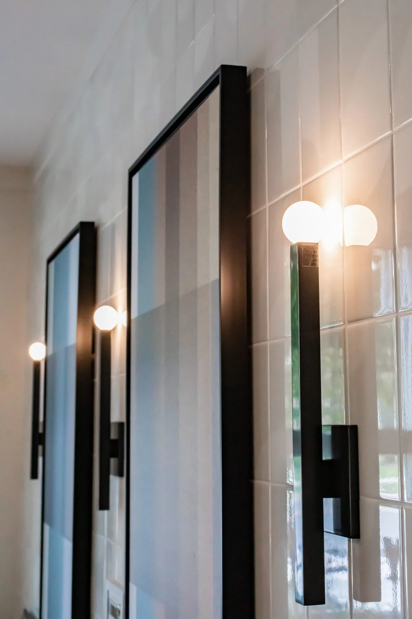 Multifamily amenity interior detail: black linear wall sconces with twin white globes between framed artworks on white tile