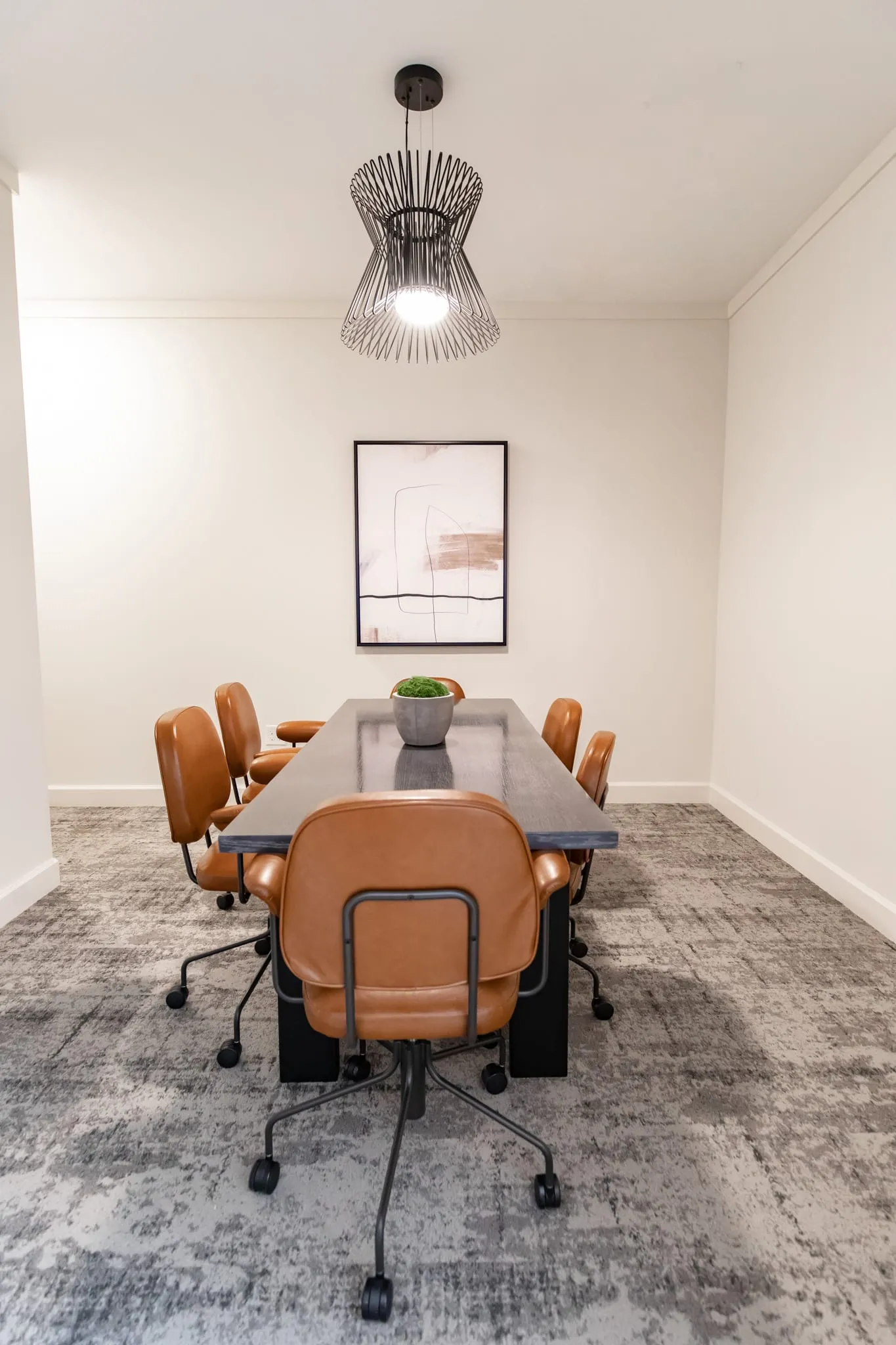 Multifamily amenity conference room with terracotta leather chairs around the table under a wire drum pendant