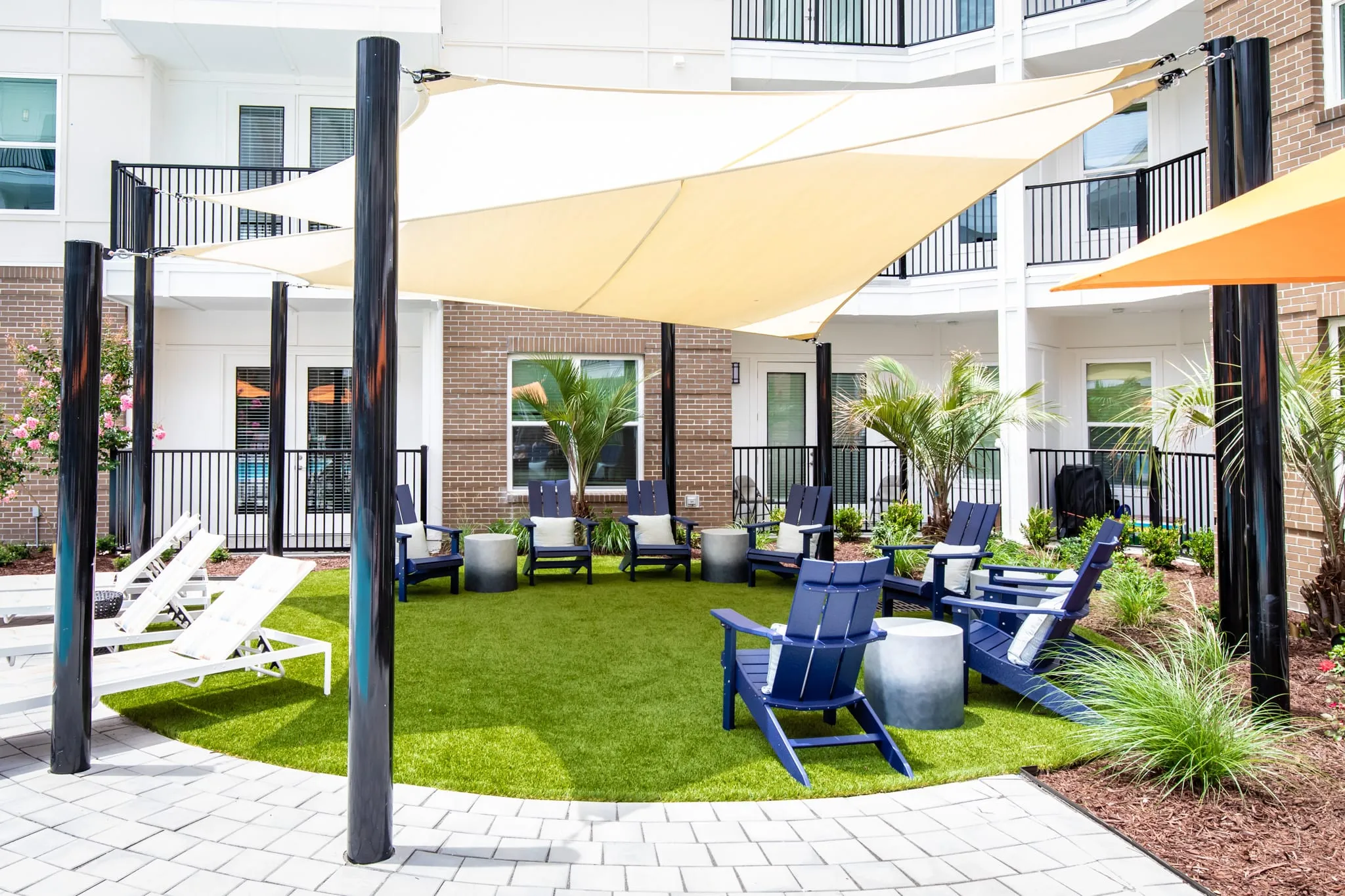 Multifamily community courtyard with shade sails above navy Adirondack chairs on the turf lawn