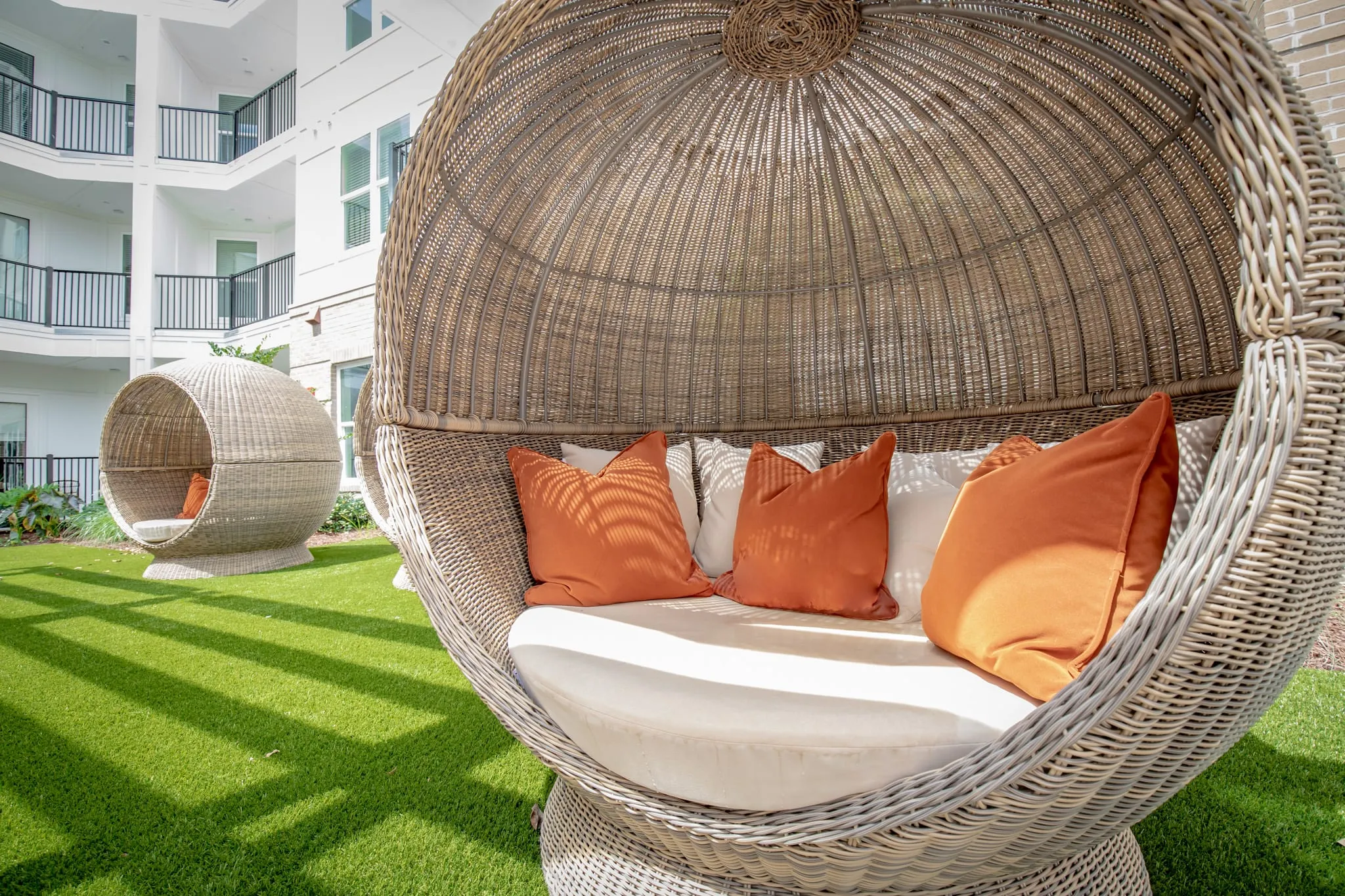 Multifamily community courtyard lawn with woven egg chairs, orange cushions inside the hanging seats