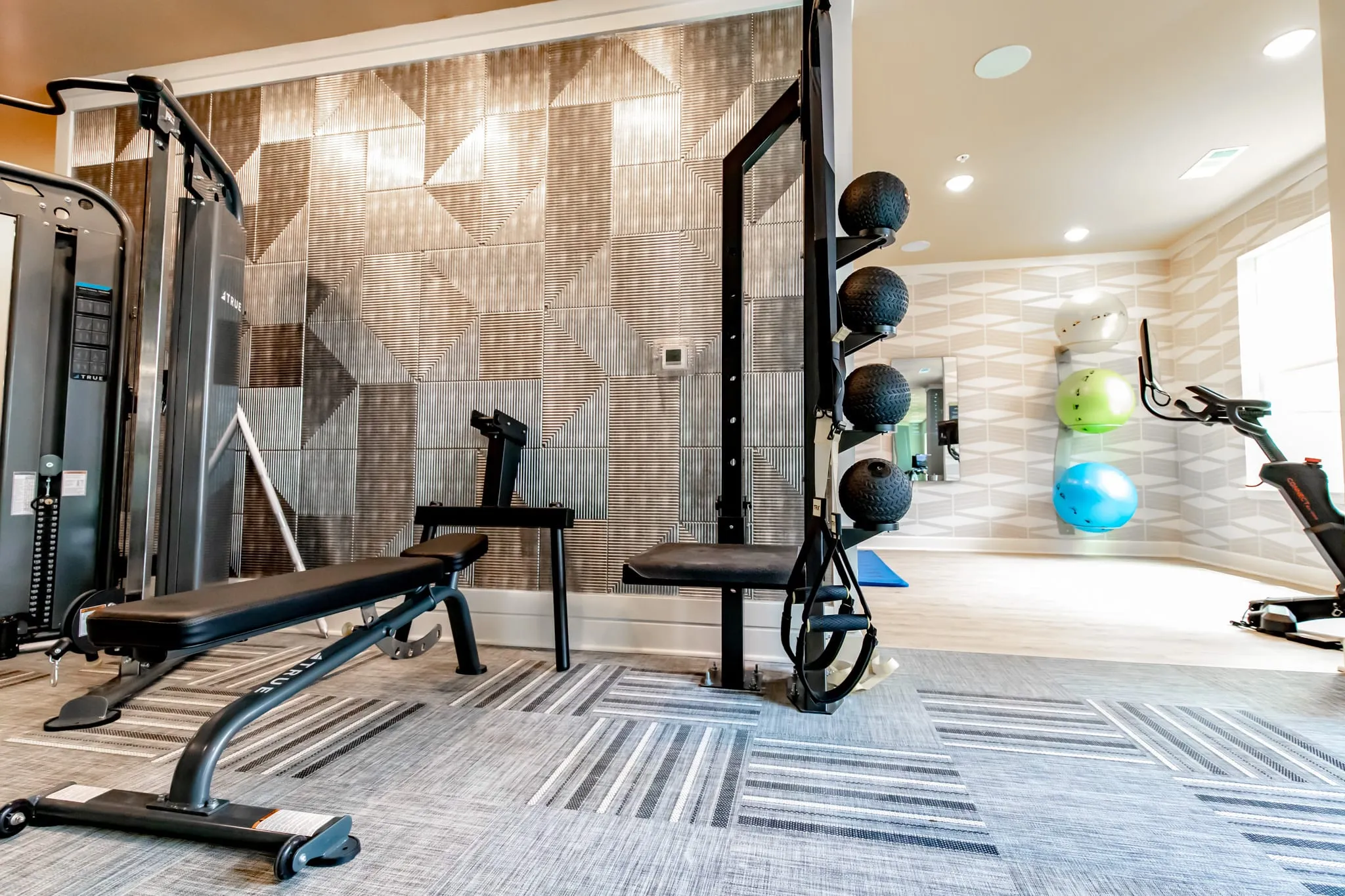 Multifamily amenity fitness center with a cable machine and free weights against a tiled feature wall