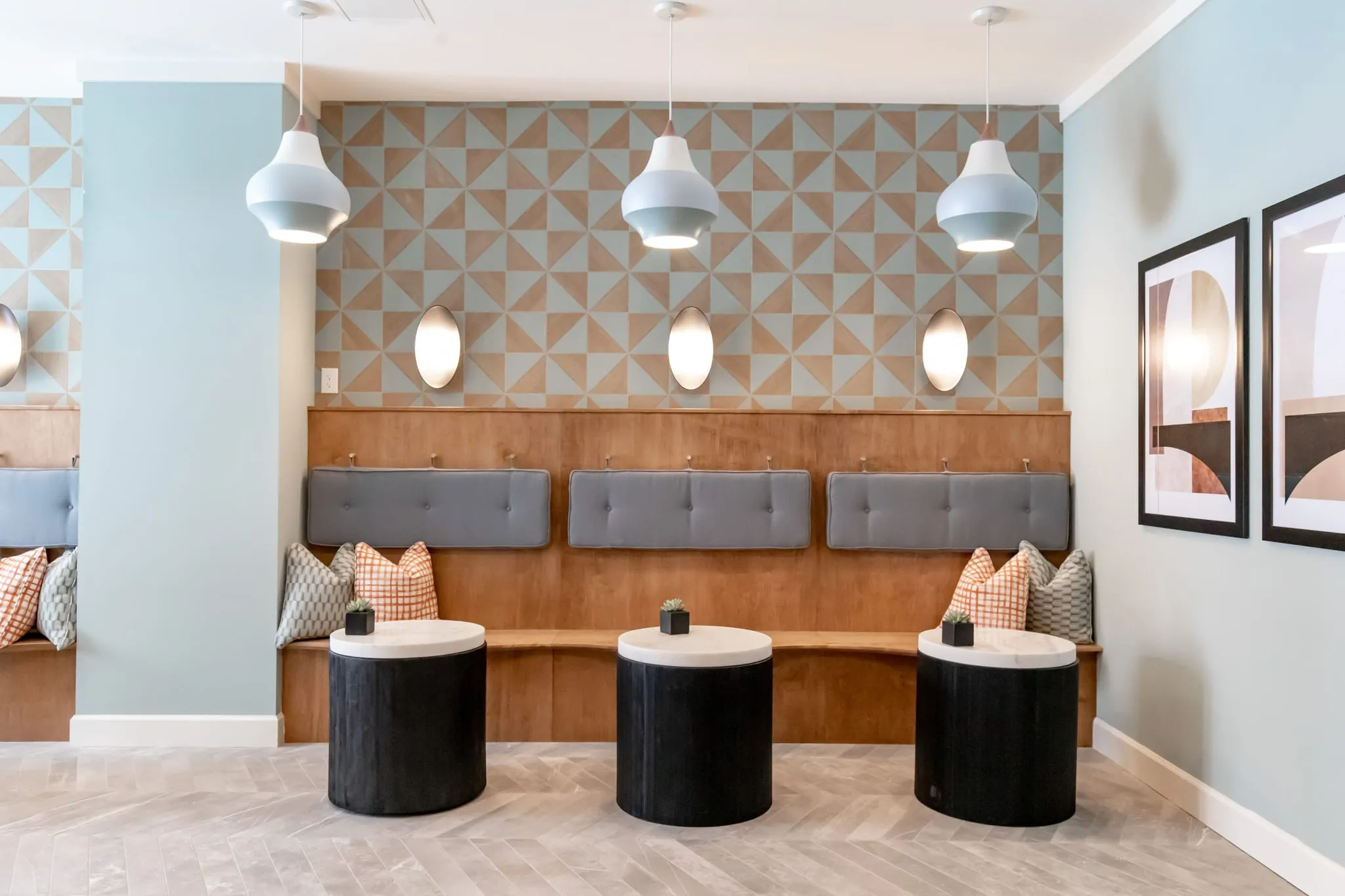 Multifamily amenity lobby banquette, a wood bench with grey cushions below geometric wallcovering and white pendants
