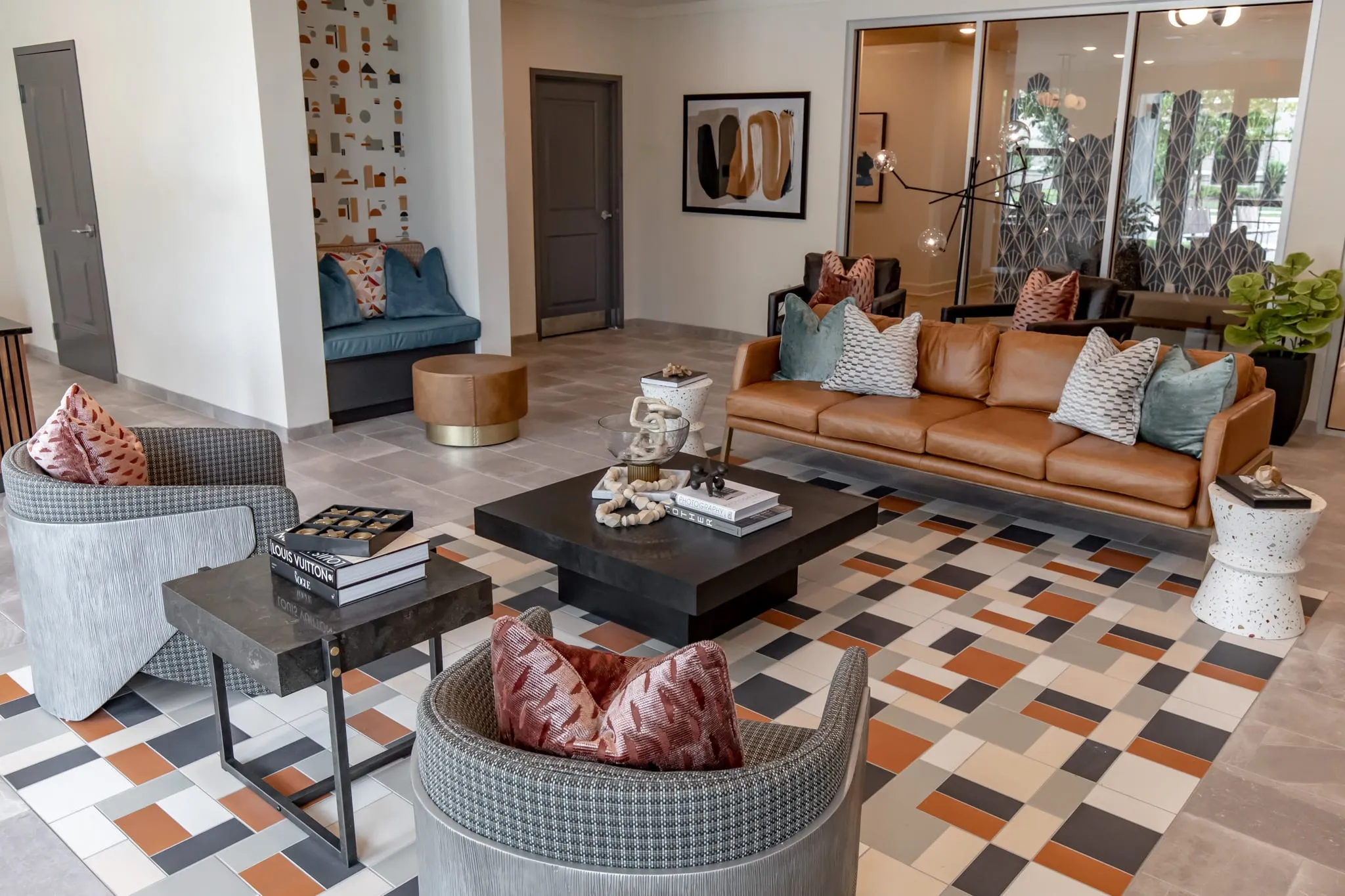 Multifamily amenity lobby lounge with a tan leather sofa, grey swivel chairs and a black coffee table on orange and grey tile