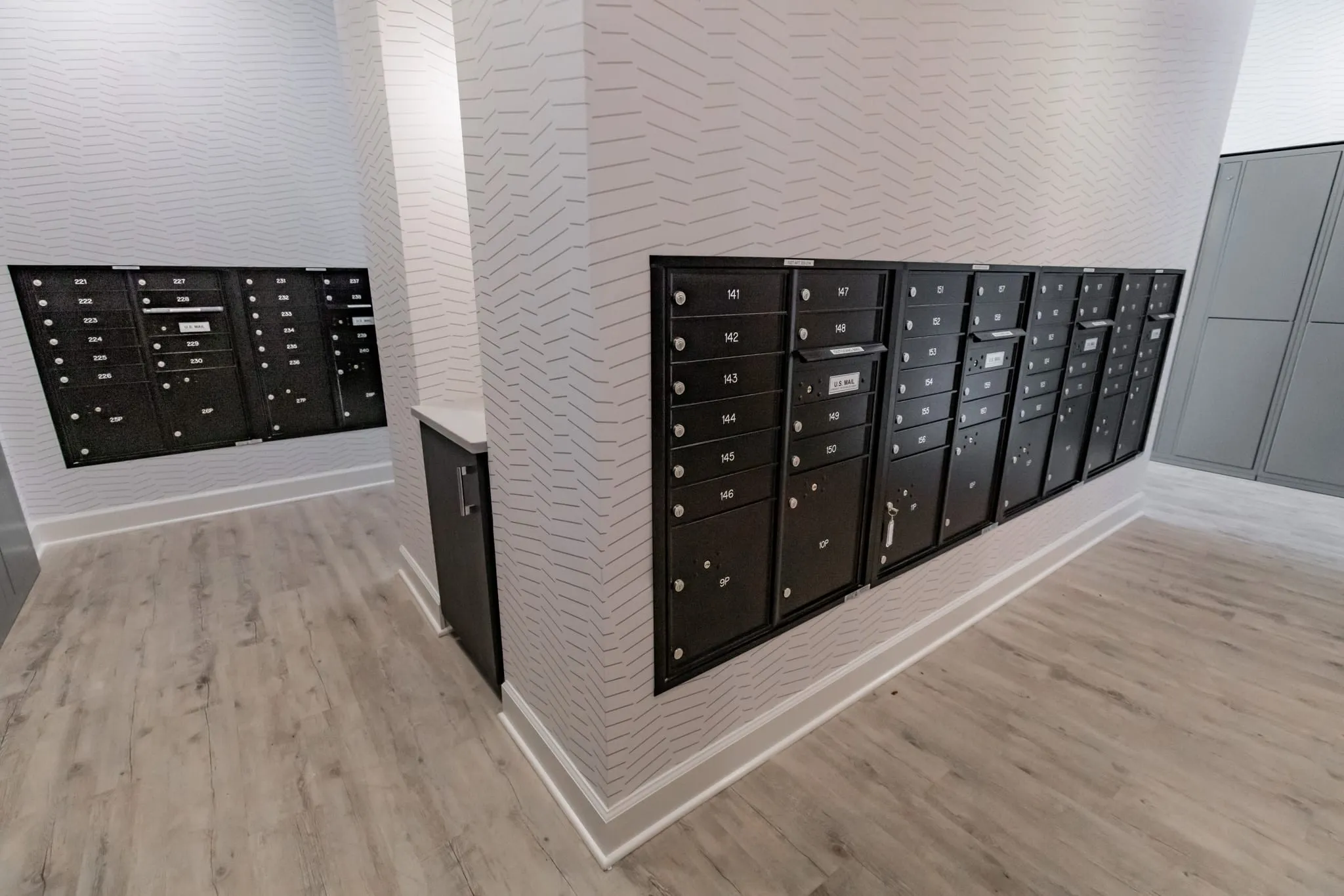 Multifamily amenity mail room with black mailboxes and grey parcel lockers set against textured white walls