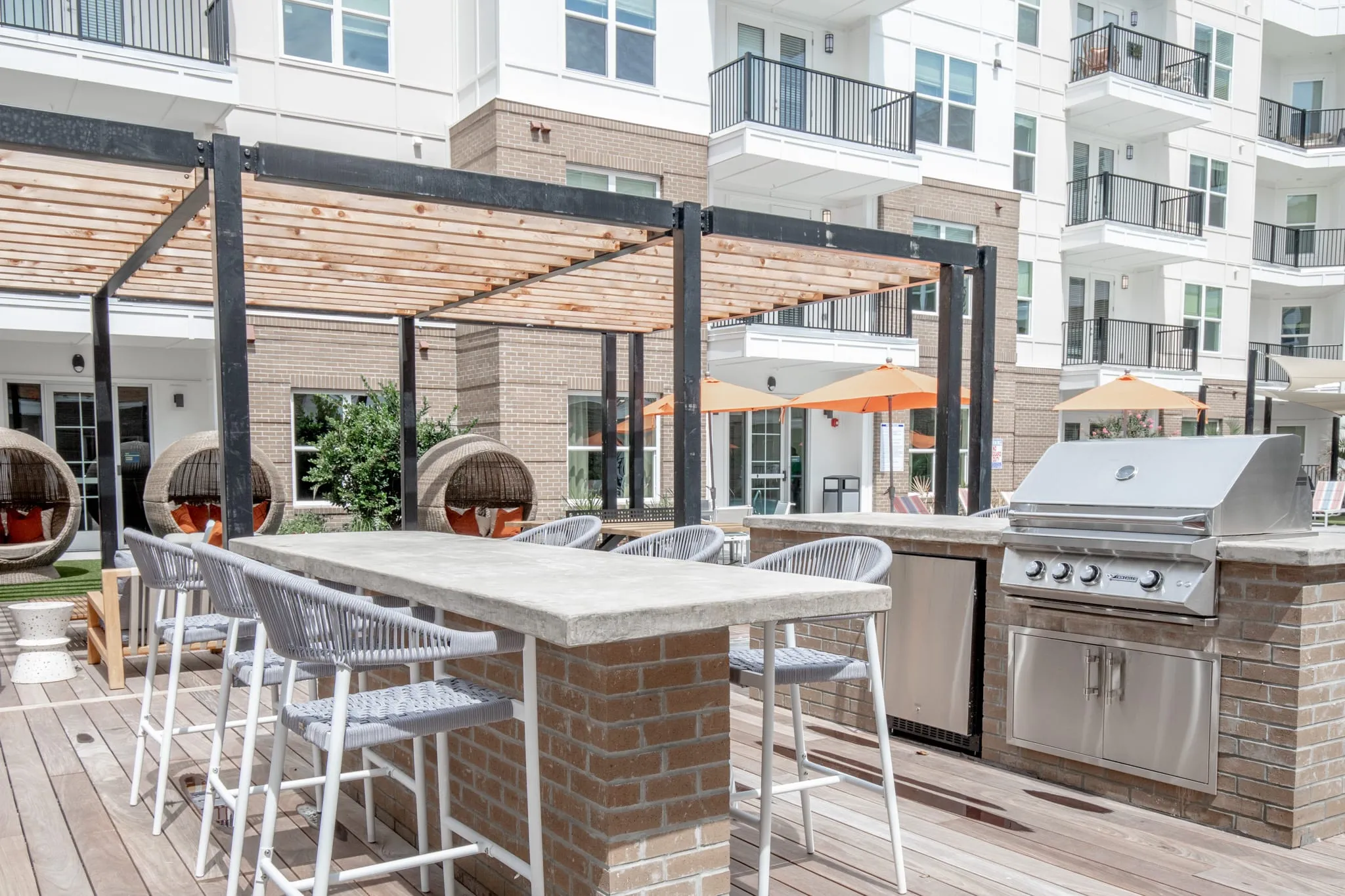 Multifamily community outdoor kitchen with a grill and a concrete-topped brick bar with woven stools by the timber pergola