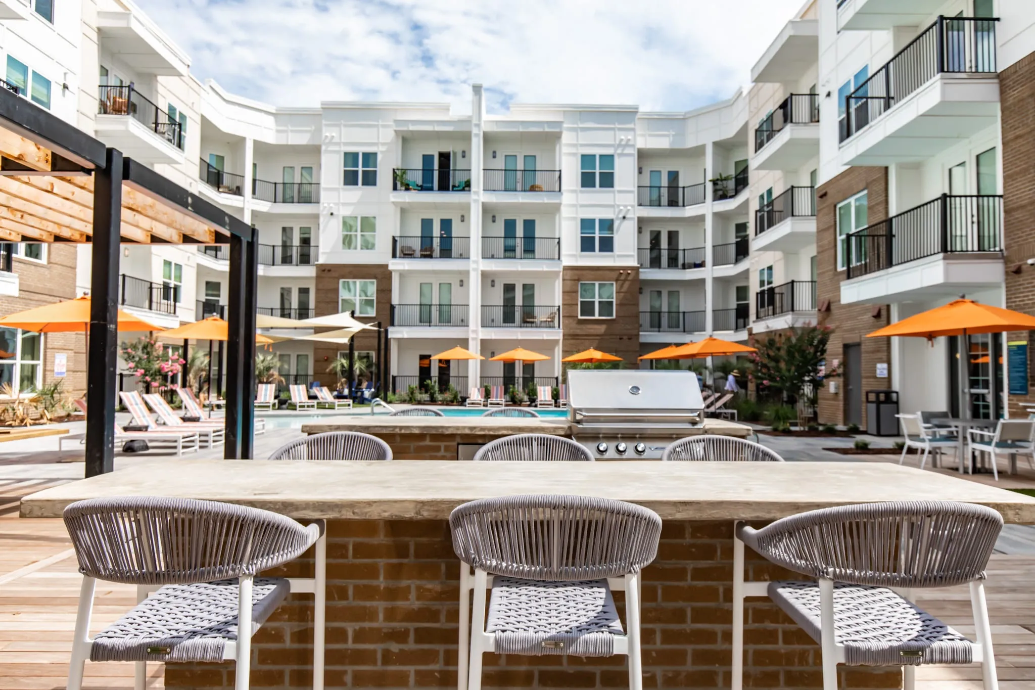 Multifamily amenity pool bar with woven stools along the brick counter overlooking the courtyard umbrellas