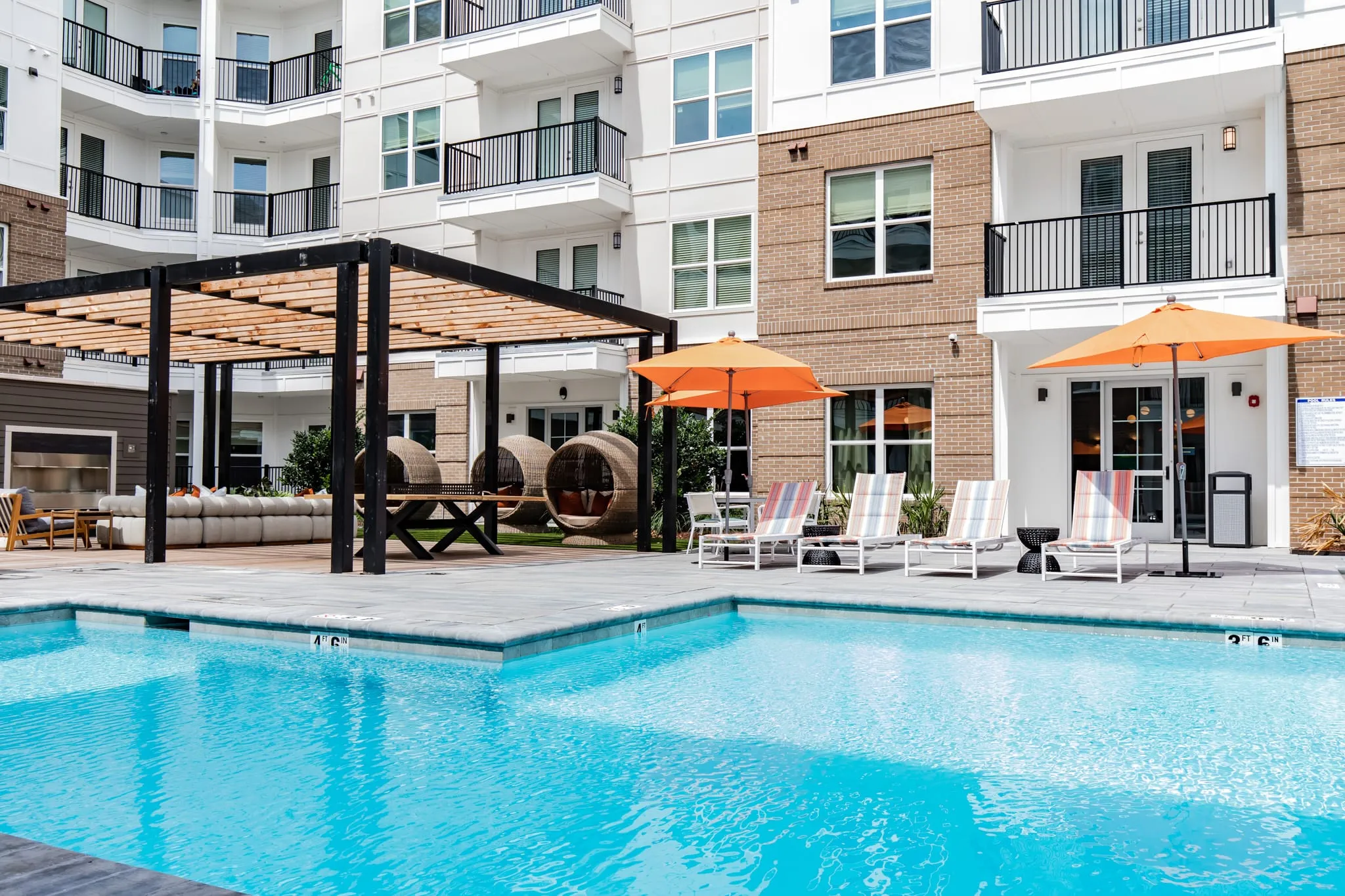 Multifamily community resort pool with orange umbrellas and timber pergolas along the water inside the courtyard