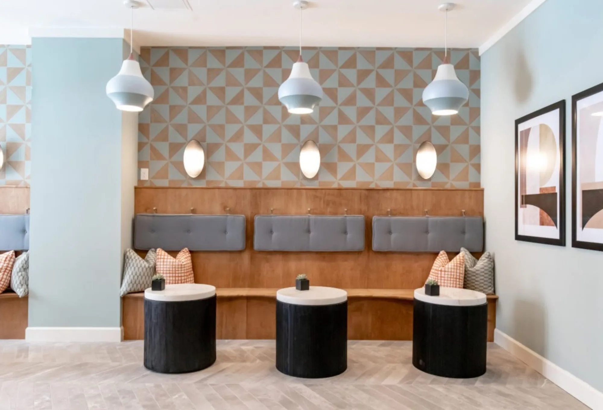 Lobby bench against a tan and blue pinwheel tile wall with oval sconces, terracotta pillows and three black drum tables