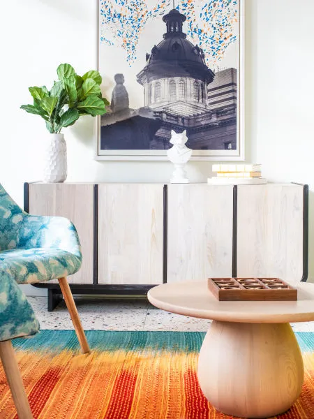 Lounge corner with a white-washed slatted credenza under a framed photograph of a domed capitol, a blue tie-dye armchair