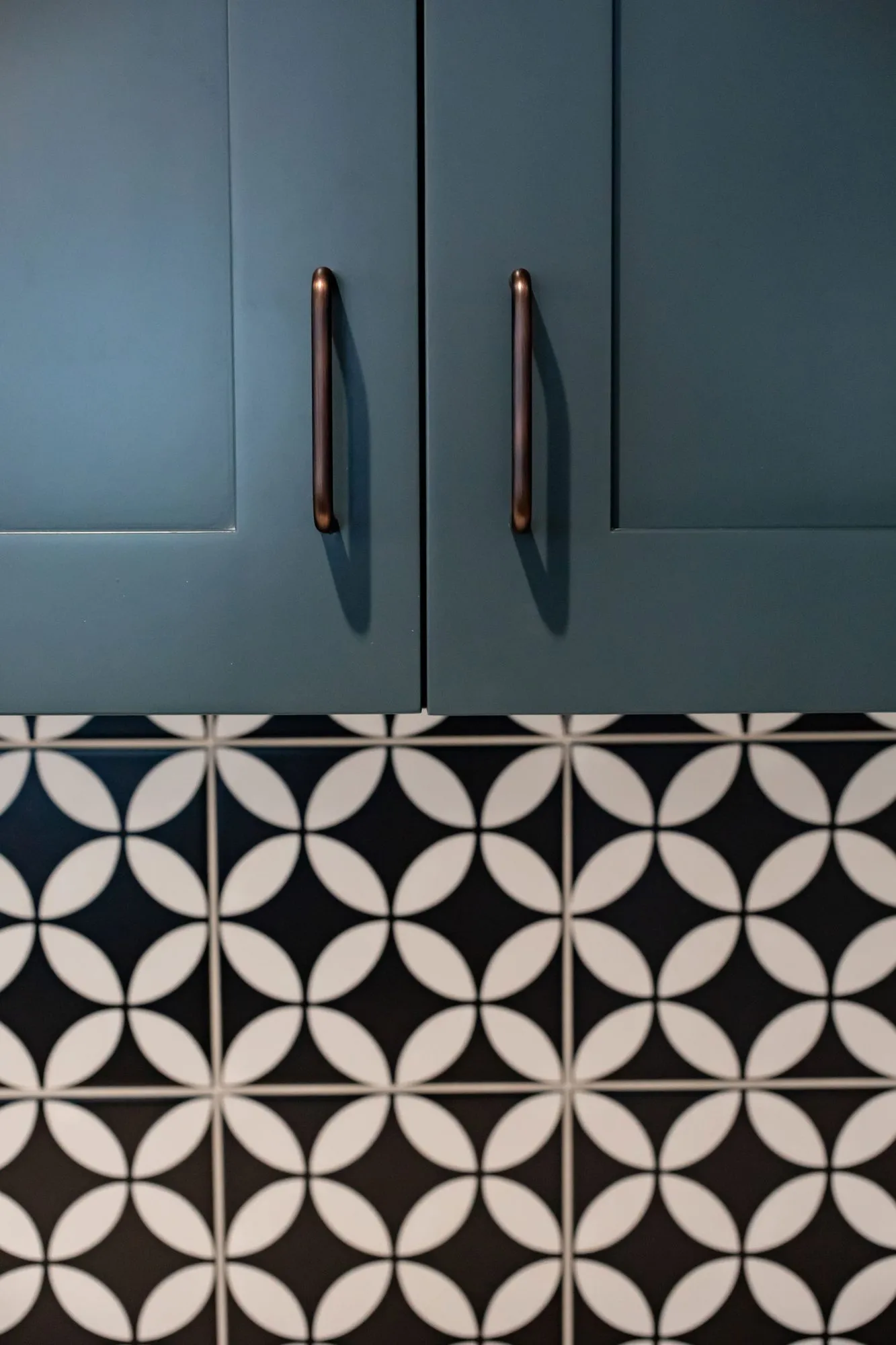 Senior living interior detail: teal cabinet doors with bronze pulls above black and white circle pattern tile