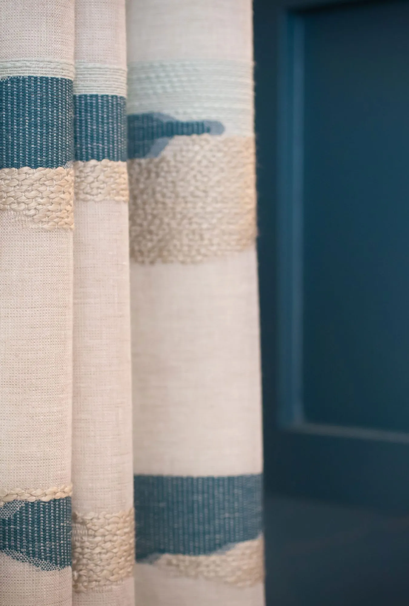 Senior living interior detail: cream drapery with blue woven stripes beside a teal door