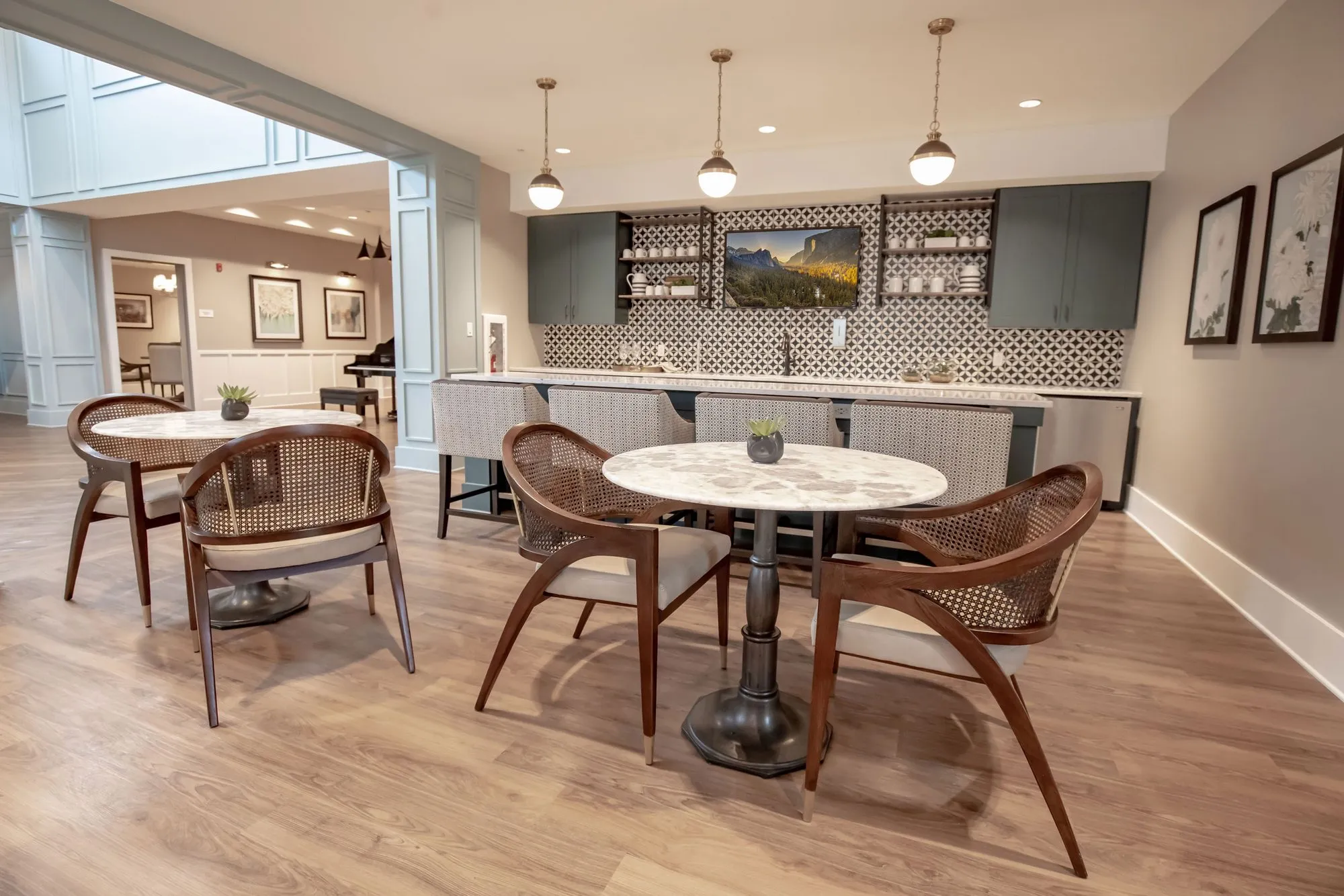 Senior living bistro seating with cane back chairs at marble tables, a bar with patterned tile and open shelves behind
