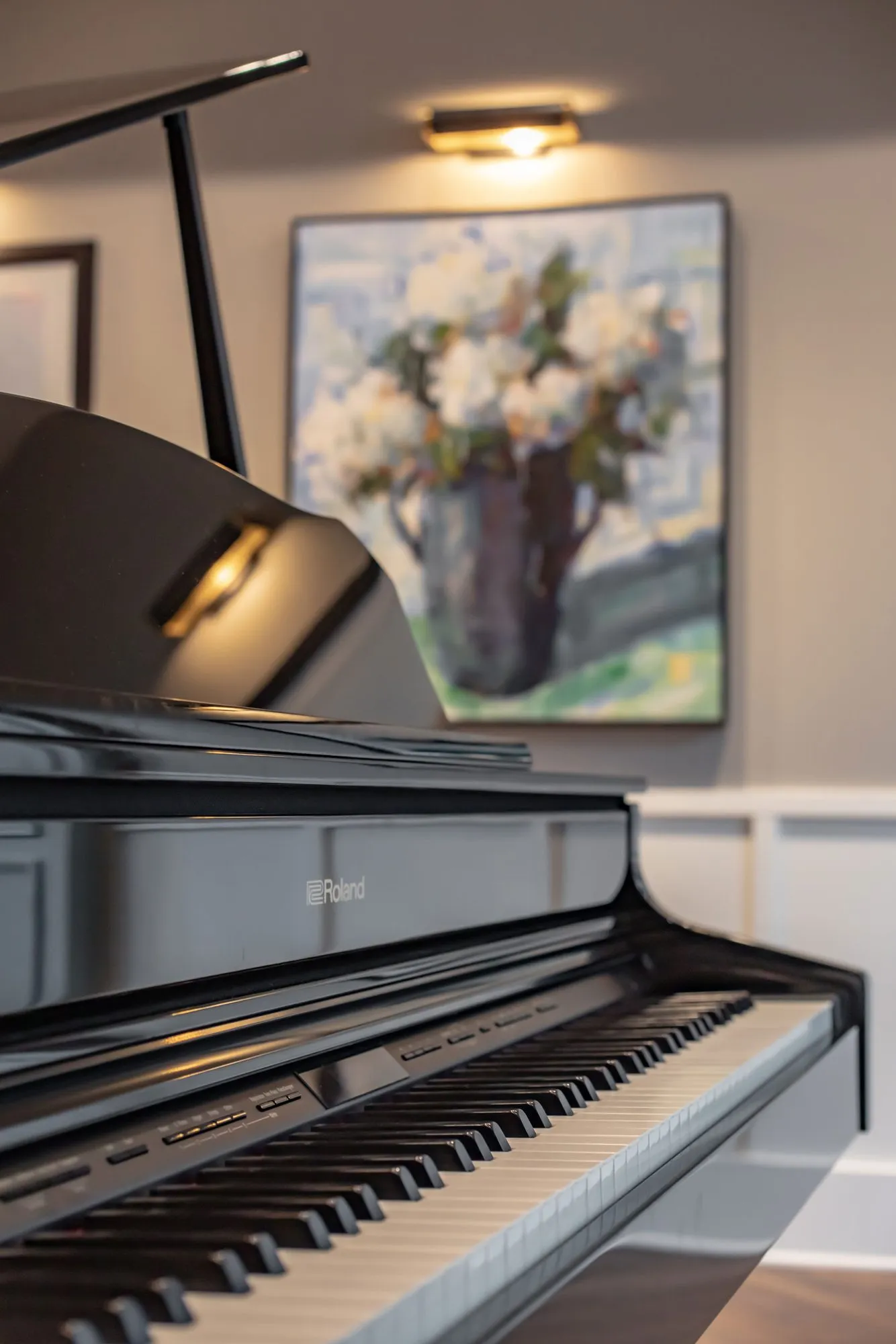 Senior living interior detail: black grand piano keyboard below a framed painting of white flowers
