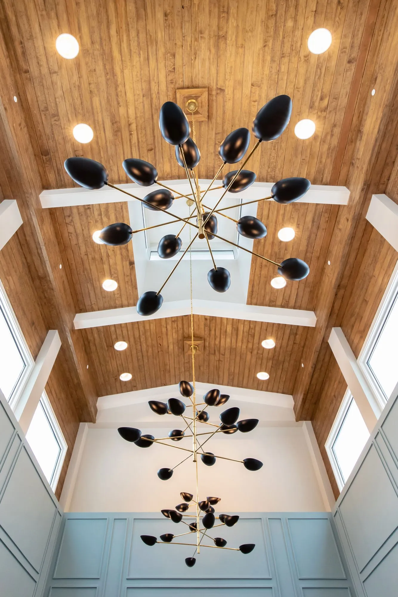 Senior living interior detail: looking up at black and brass sputnik chandeliers in a two storey space with a plank ceiling