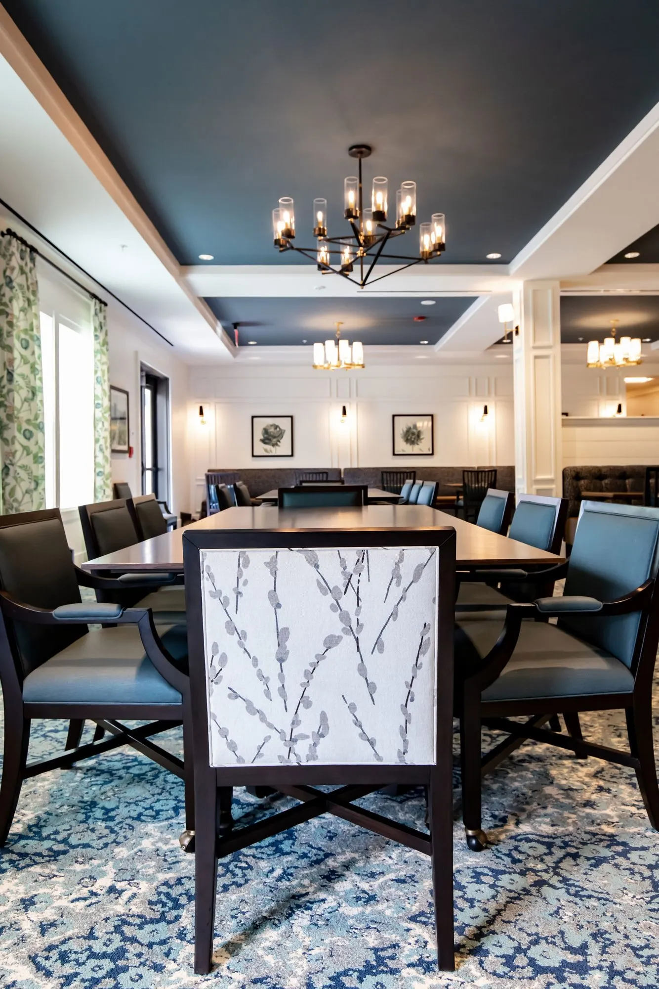 Senior living dining room, a chair with a branch print back at a table under a navy coffered ceiling