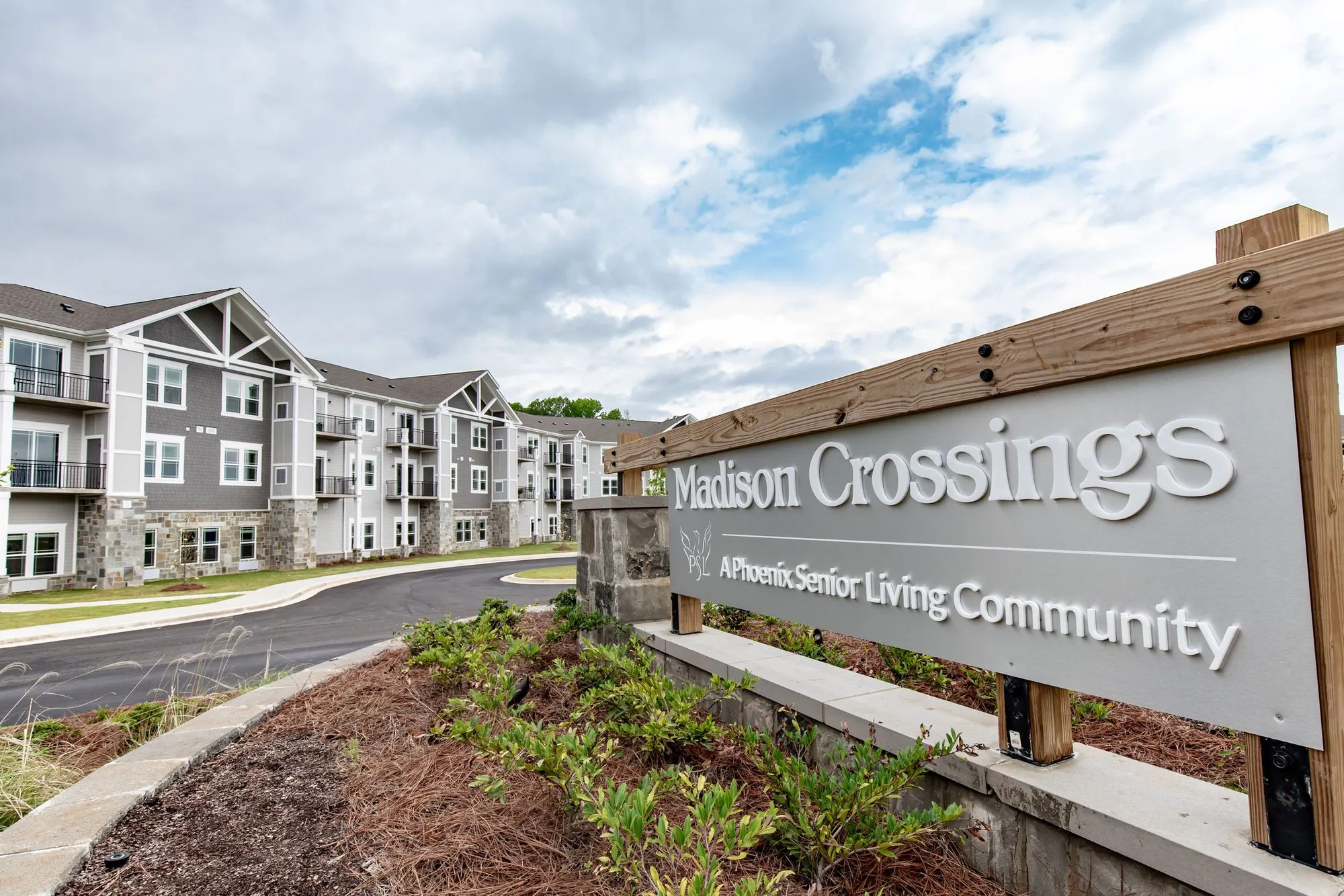 Senior living community exterior: monument sign with timber posts at the entrance drive, three storey gabled residences