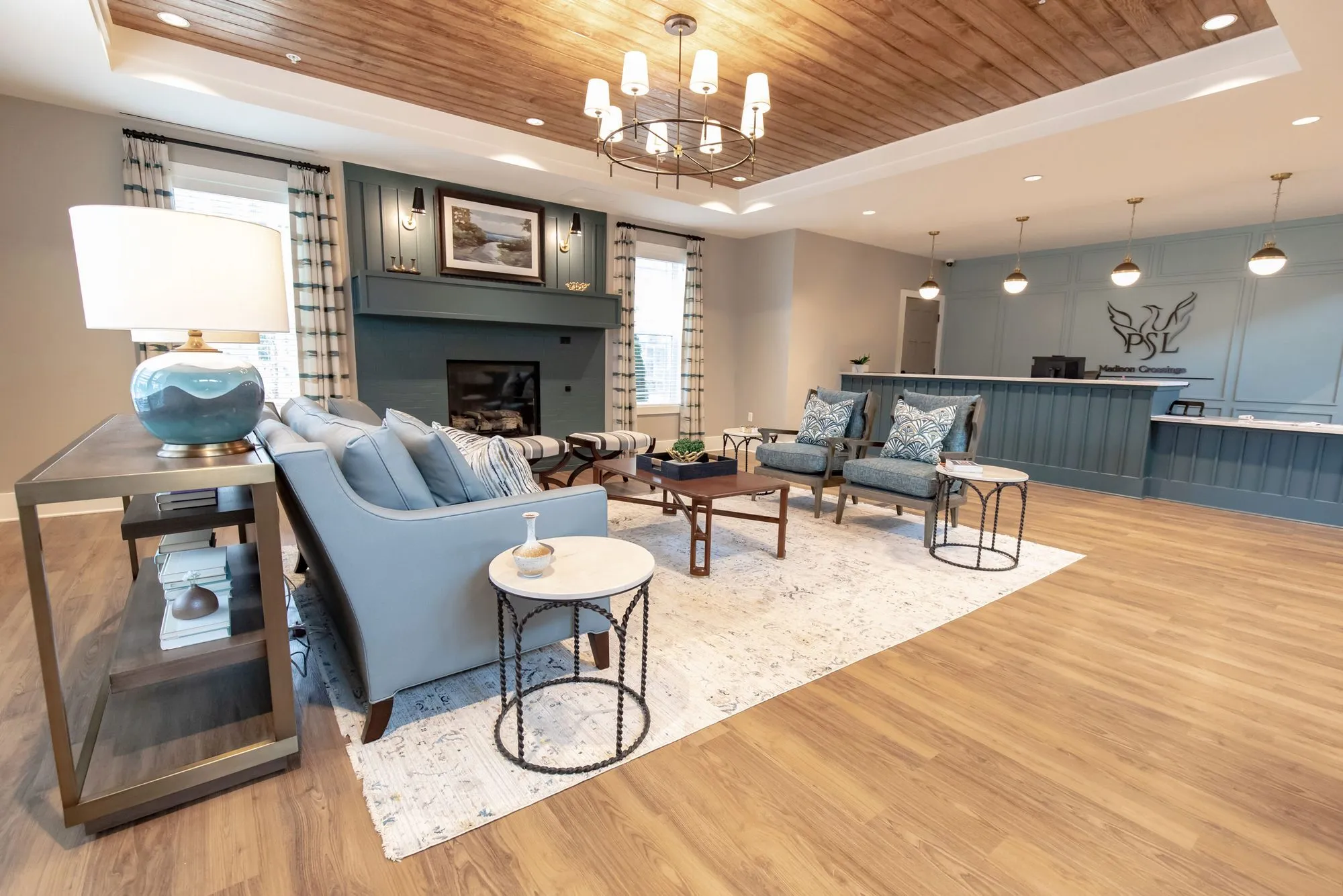 Senior living lobby with a slate blue fireplace wall, grey sofa and wood plank tray ceiling, reception desk beyond