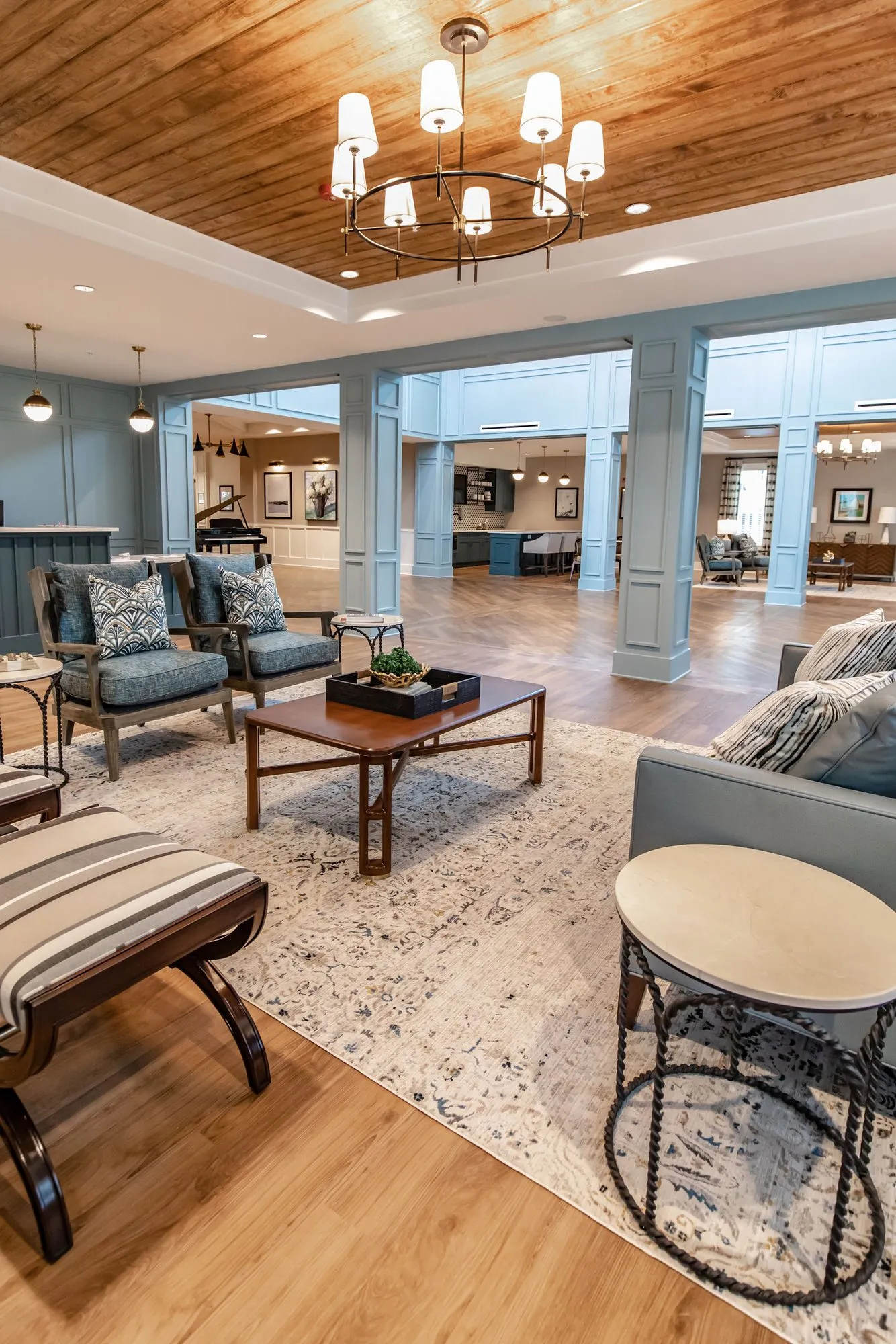 Senior living lobby sitting area with teal armchairs, a striped bench and a wood plank ceiling with chandelier