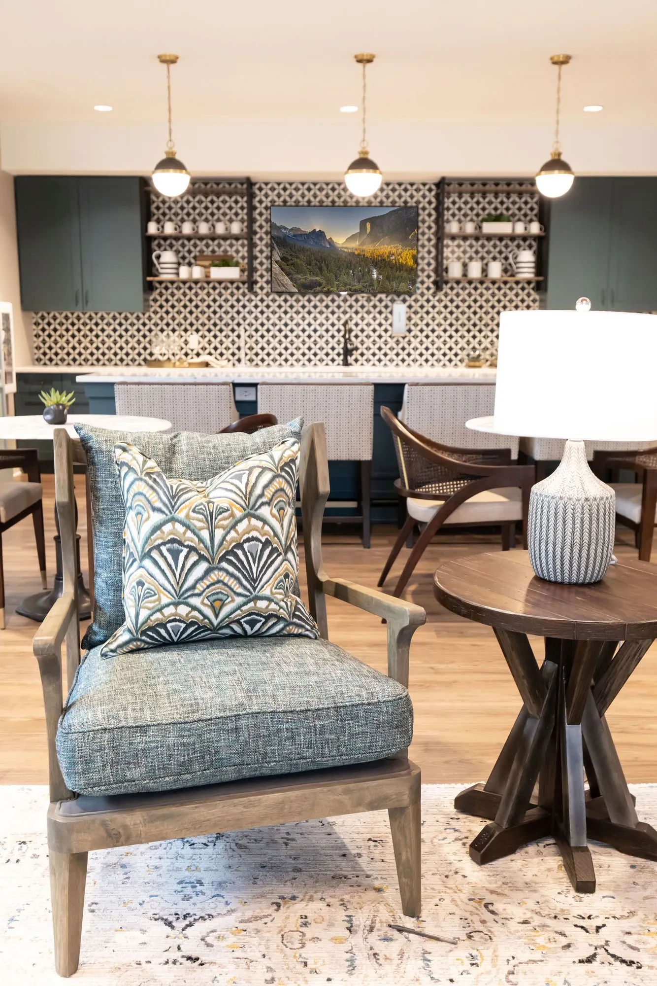 Senior living bistro: upholstered armchair with a fan pattern pillow beside a lamp table, the bar with patterned tile behind