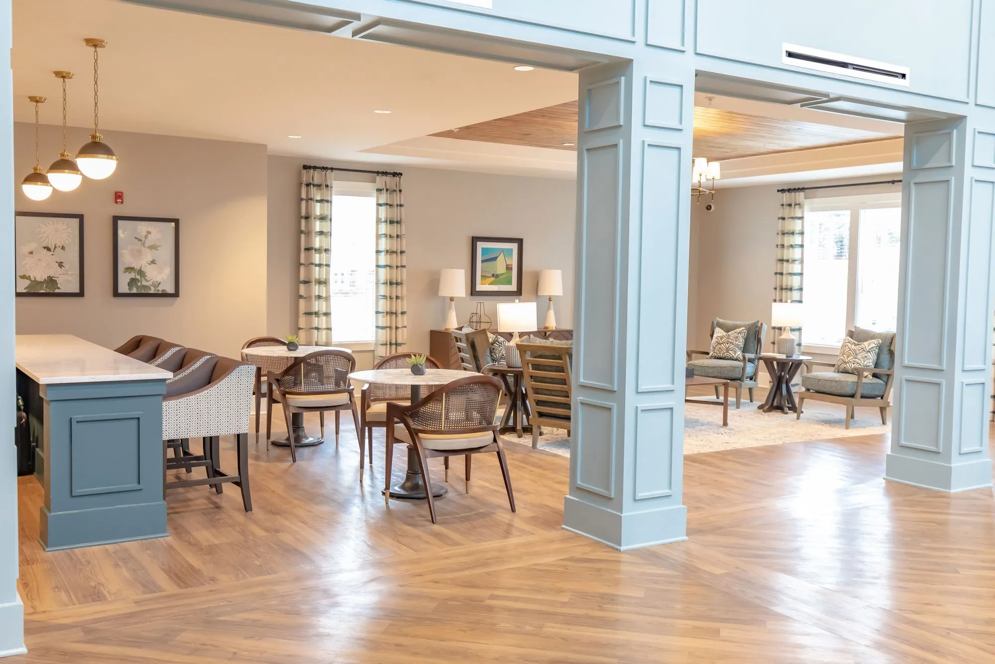 Senior living bistro area with a teal island and barstools, cane chairs at round tables between pale blue columns