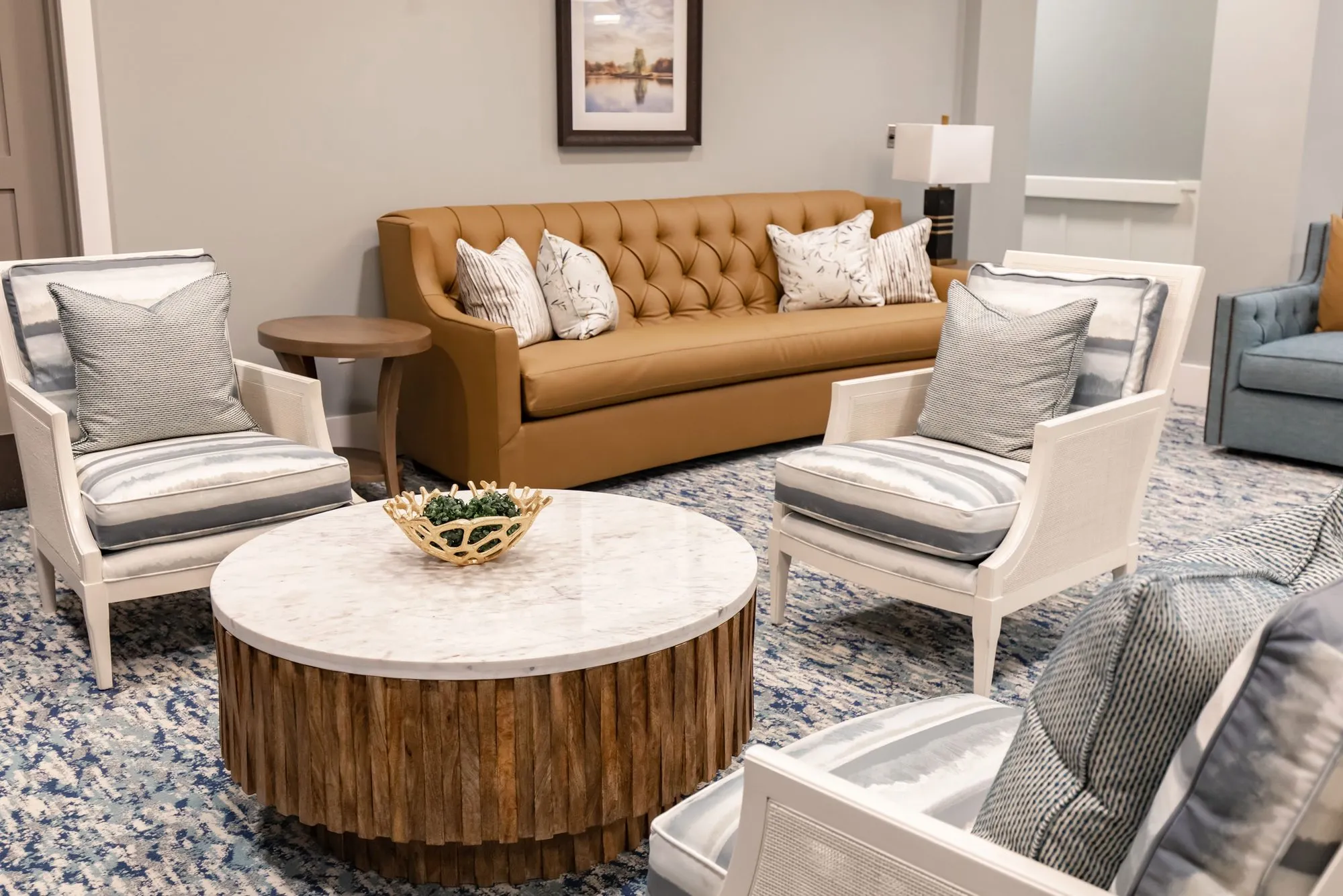 Senior living sitting area with a camel tufted leather sofa, white cane armchairs and a round marble table on a wood base