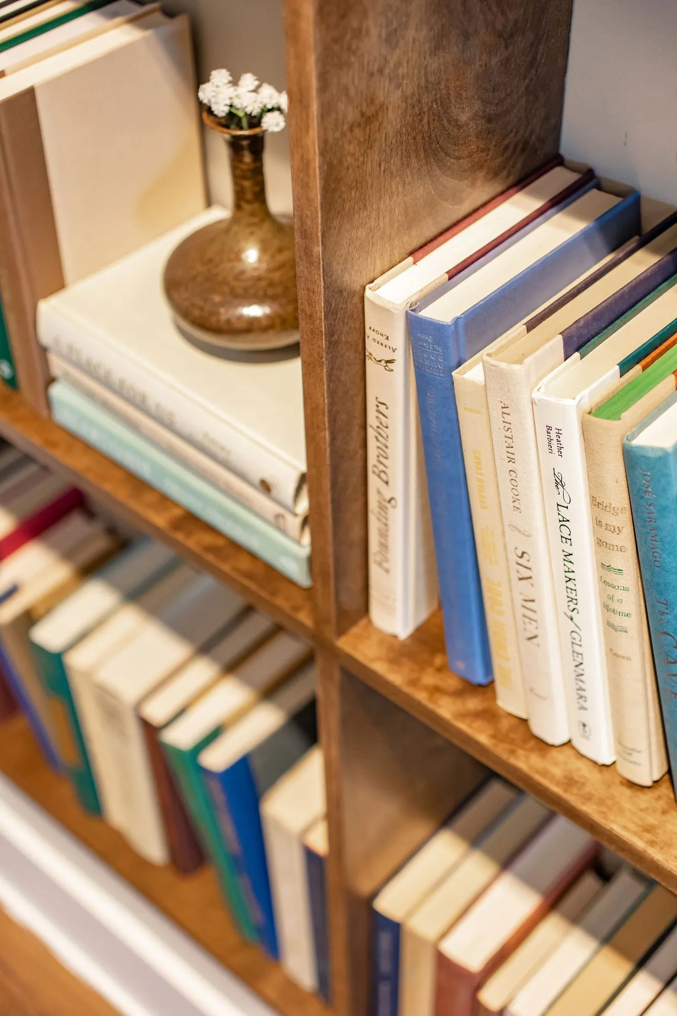 Senior living interior detail: wood bookshelves with hardback books and a bronze vase of white flowers