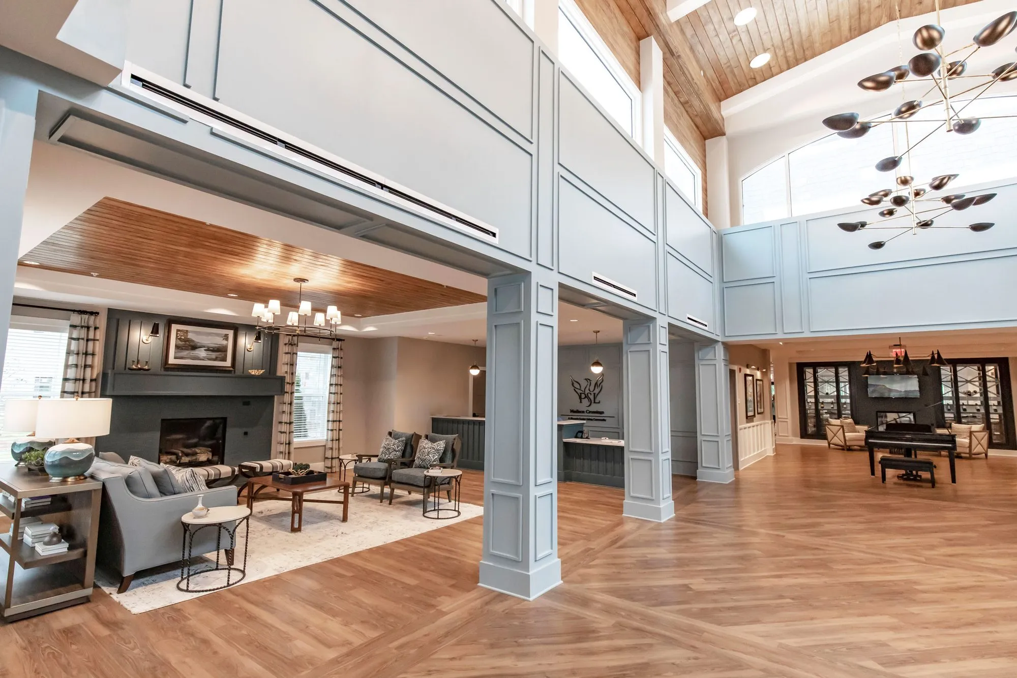 Senior living lobby with pale blue columns, the fireplace seating, a piano and dark shelving at the back