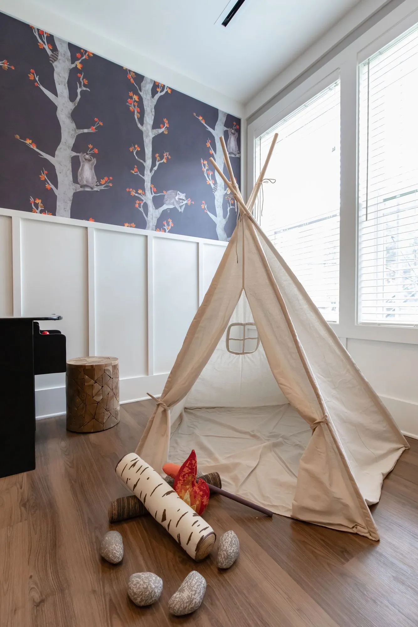 Senior living interior detail: canvas teepee and play campfire below tree wallpaper beside the windows