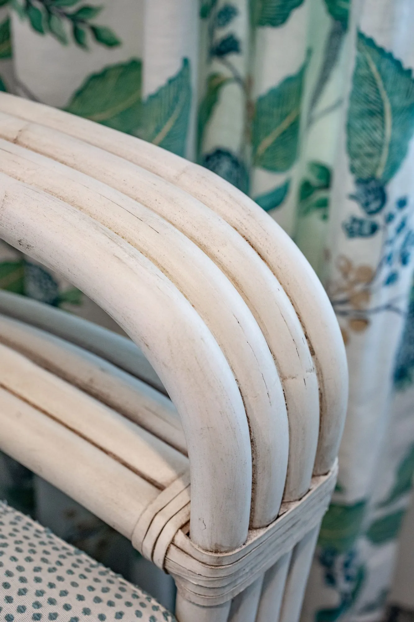 Senior living interior detail: whitewashed bent rattan chair arm against green leaf print drapery