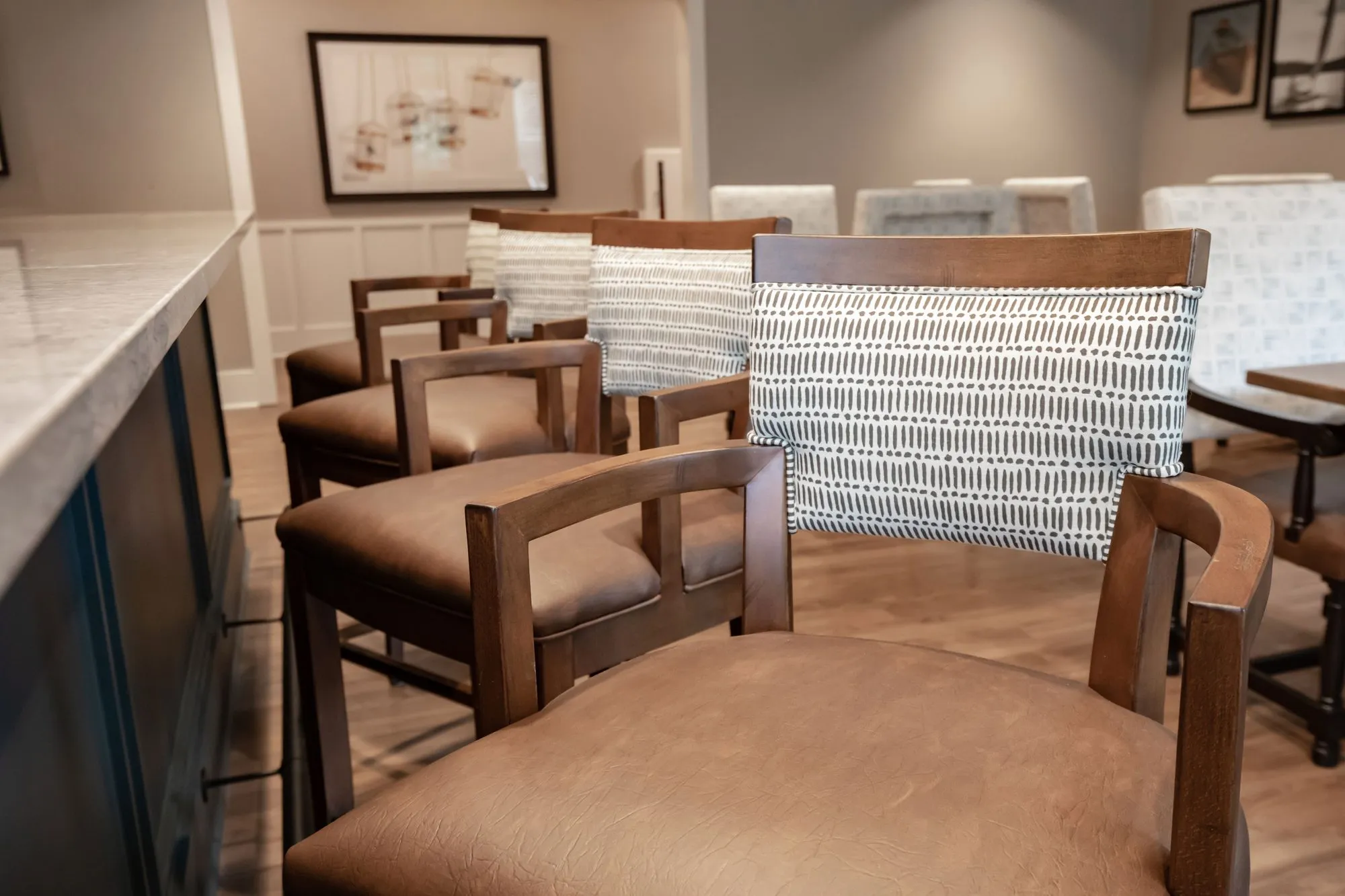 Senior living interior detail: wood barstools with leather seats and patterned backs along a counter