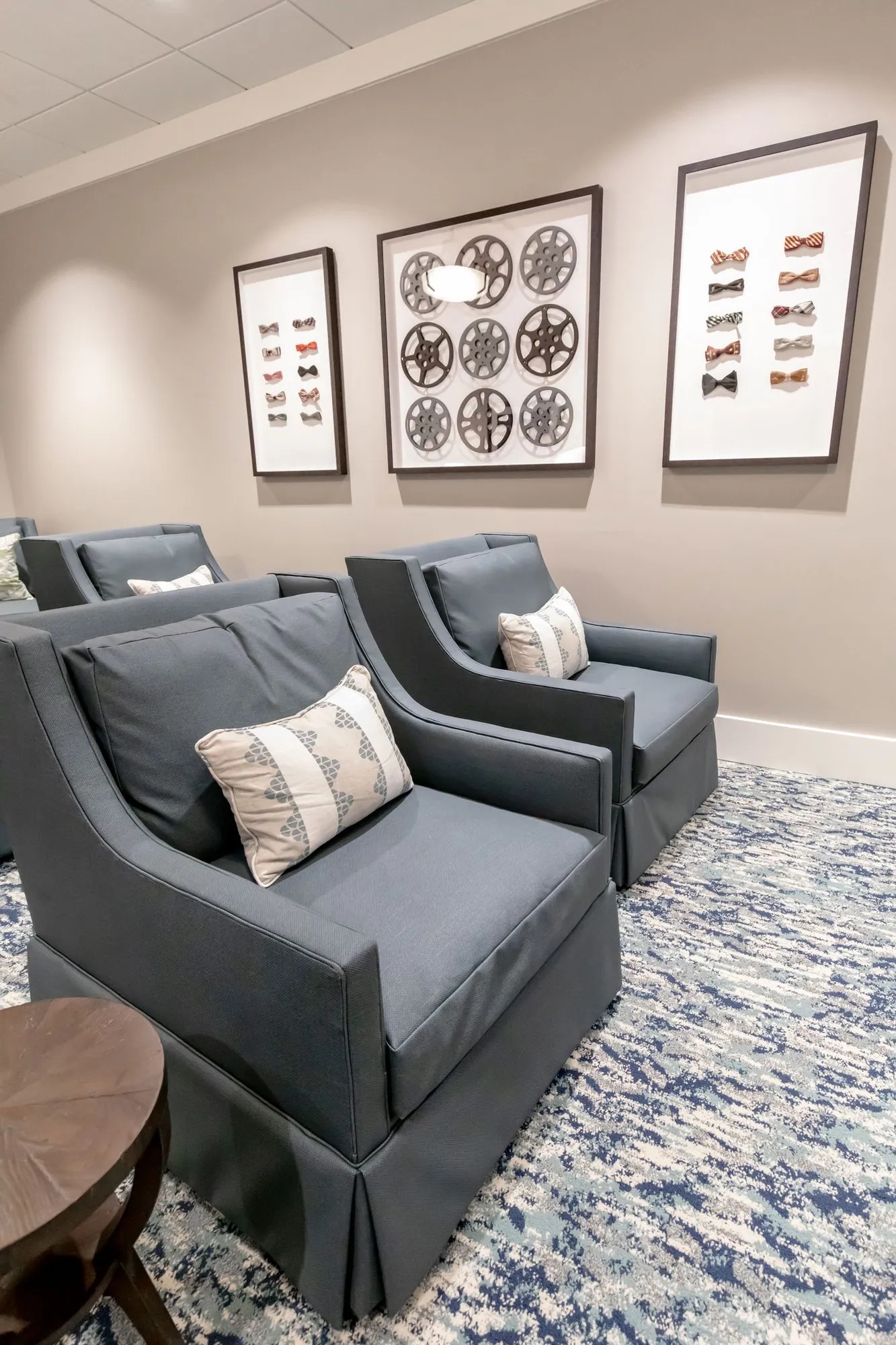 Senior living theatre seating: slate blue skirted armchairs below three framed shadow boxes, one of film reels