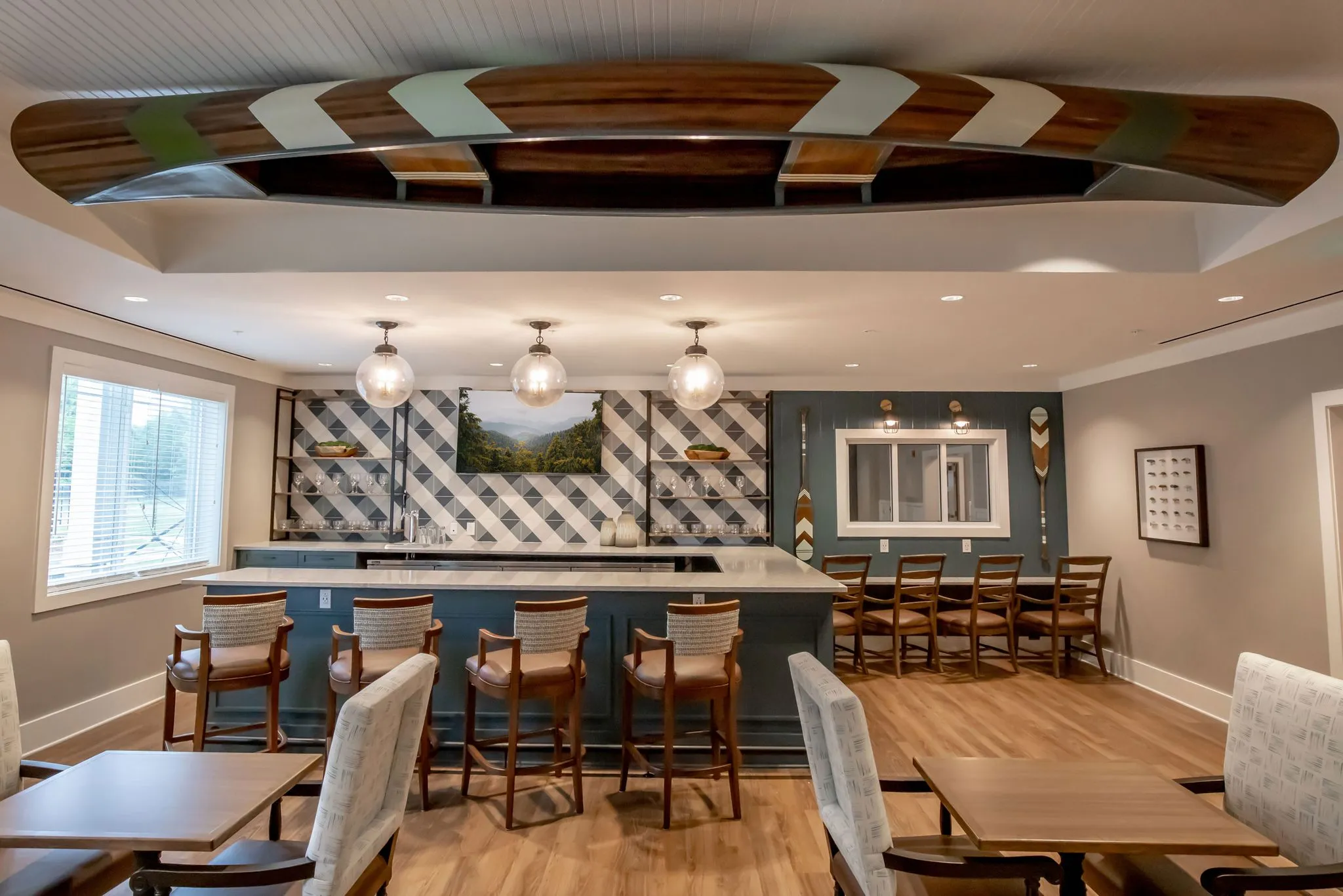 Senior living bistro with a wooden canoe mounted overhead and globe pendants above the harlequin tiled bar