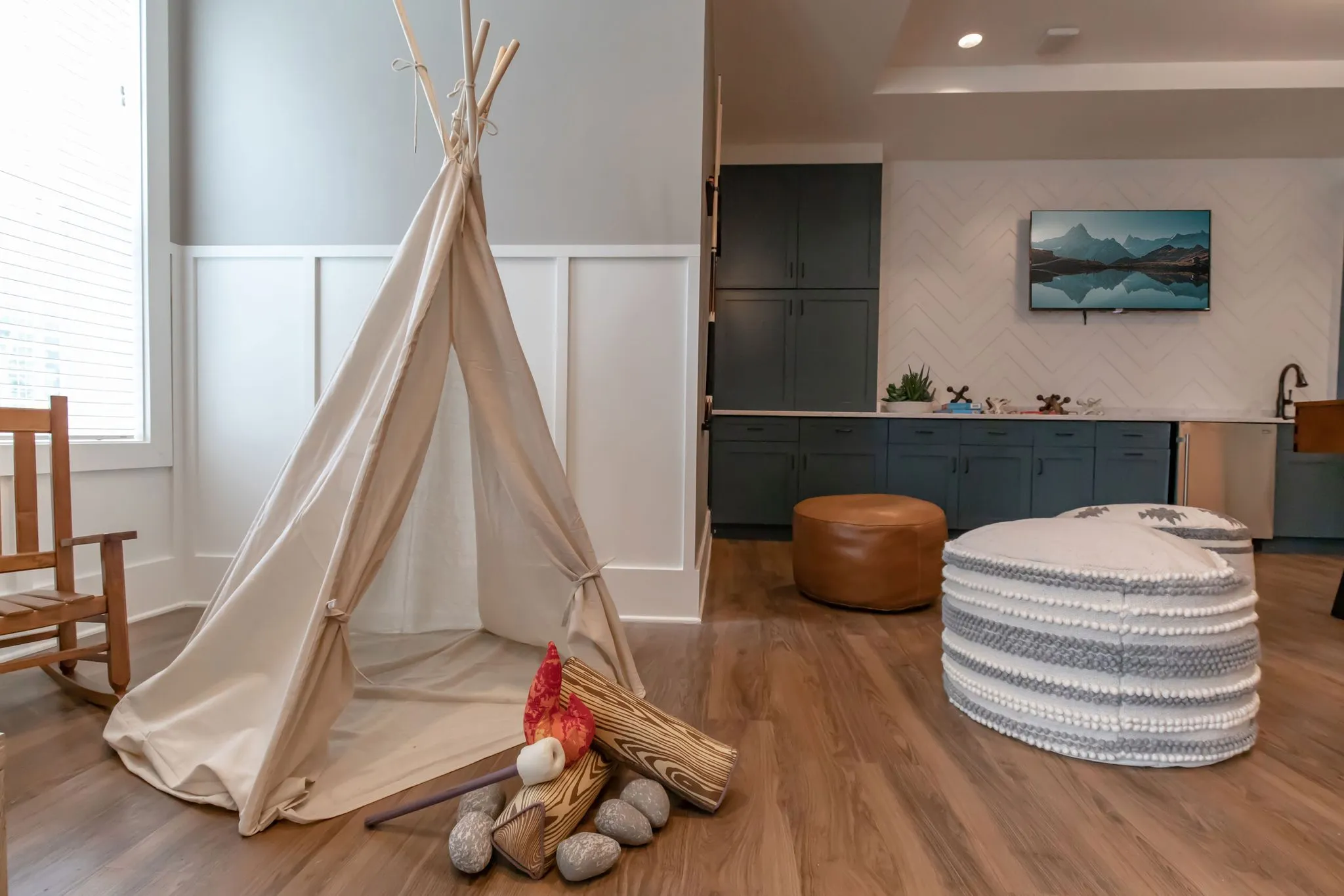 Senior living kids corner with a canvas teepee and make-believe campfire beside teal cabinetry and woven poufs