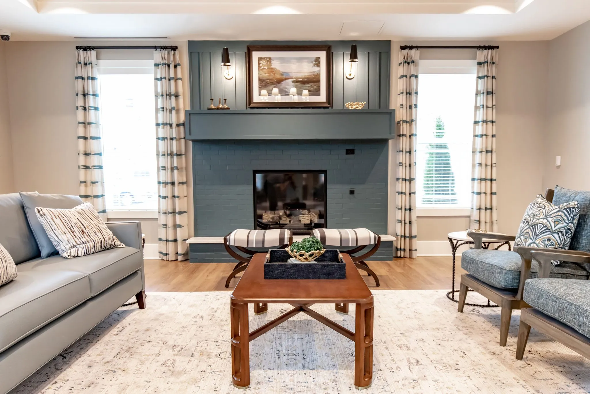 Senior living community living room with a blue-grey shiplap fireplace between striped drapery, a grey sofa facing it