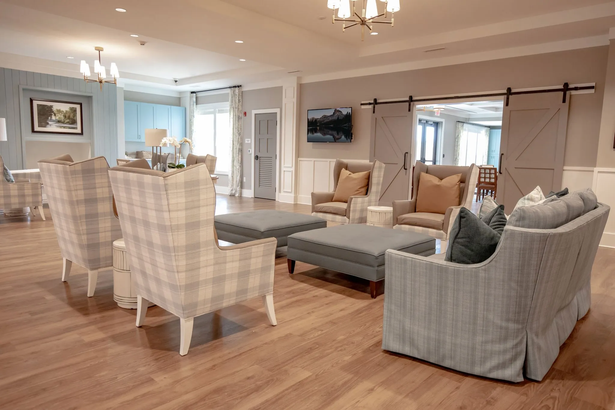 Senior living living room with plaid wing chairs and grey ottomans before sliding barn doors
