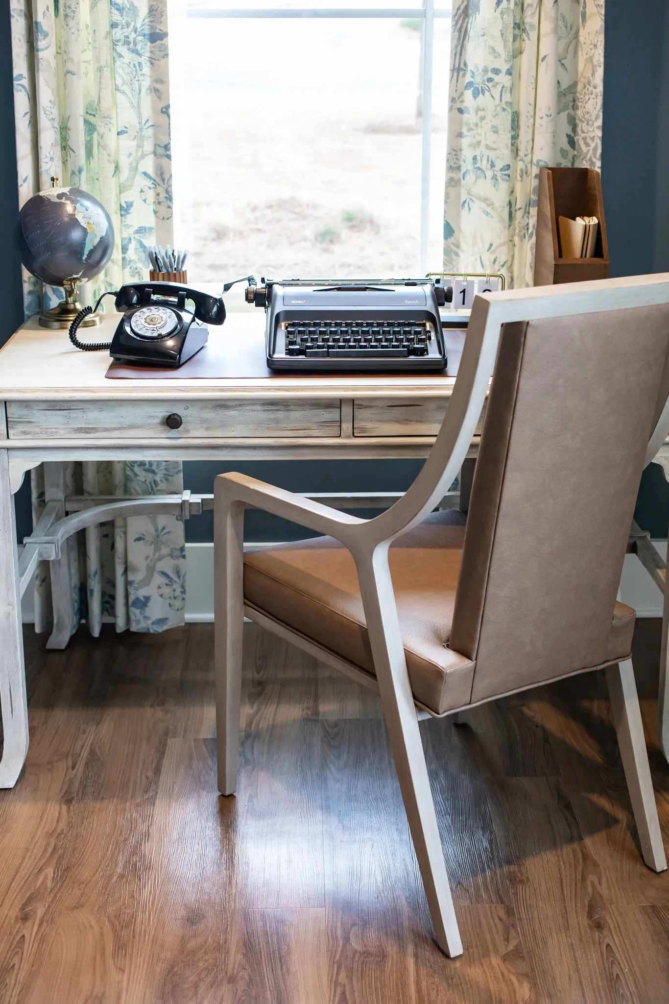 Senior living interior detail: a rotary telephone, typewriter and globe on a whitewashed writing desk