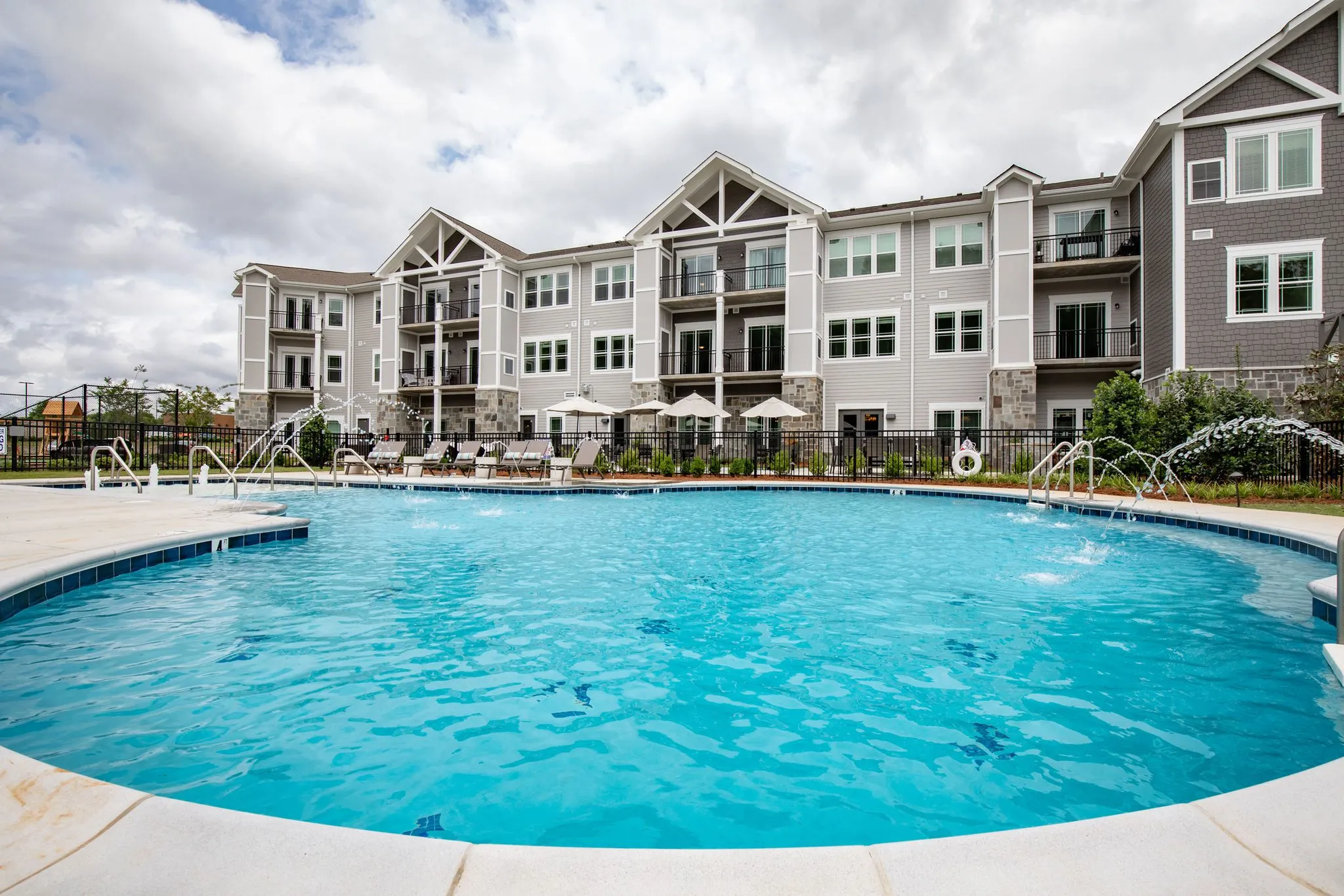Senior living pool with fountain jets arcing across the water, the gabled residences behind