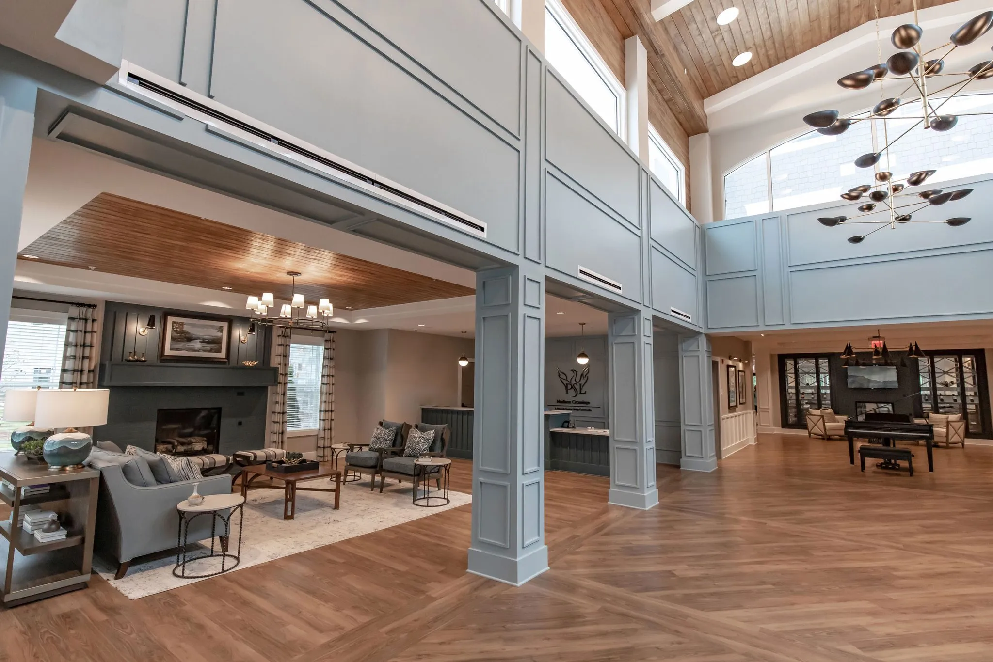 Senior living lobby under sputnik chandeliers, pale blue paneled columns opening to a fireplace sitting area and a piano
