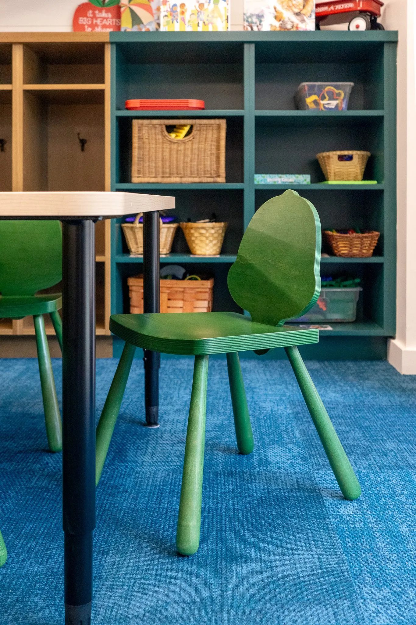 School classroom chair with a green back shaped like an acorn, at a table beside teal shelving