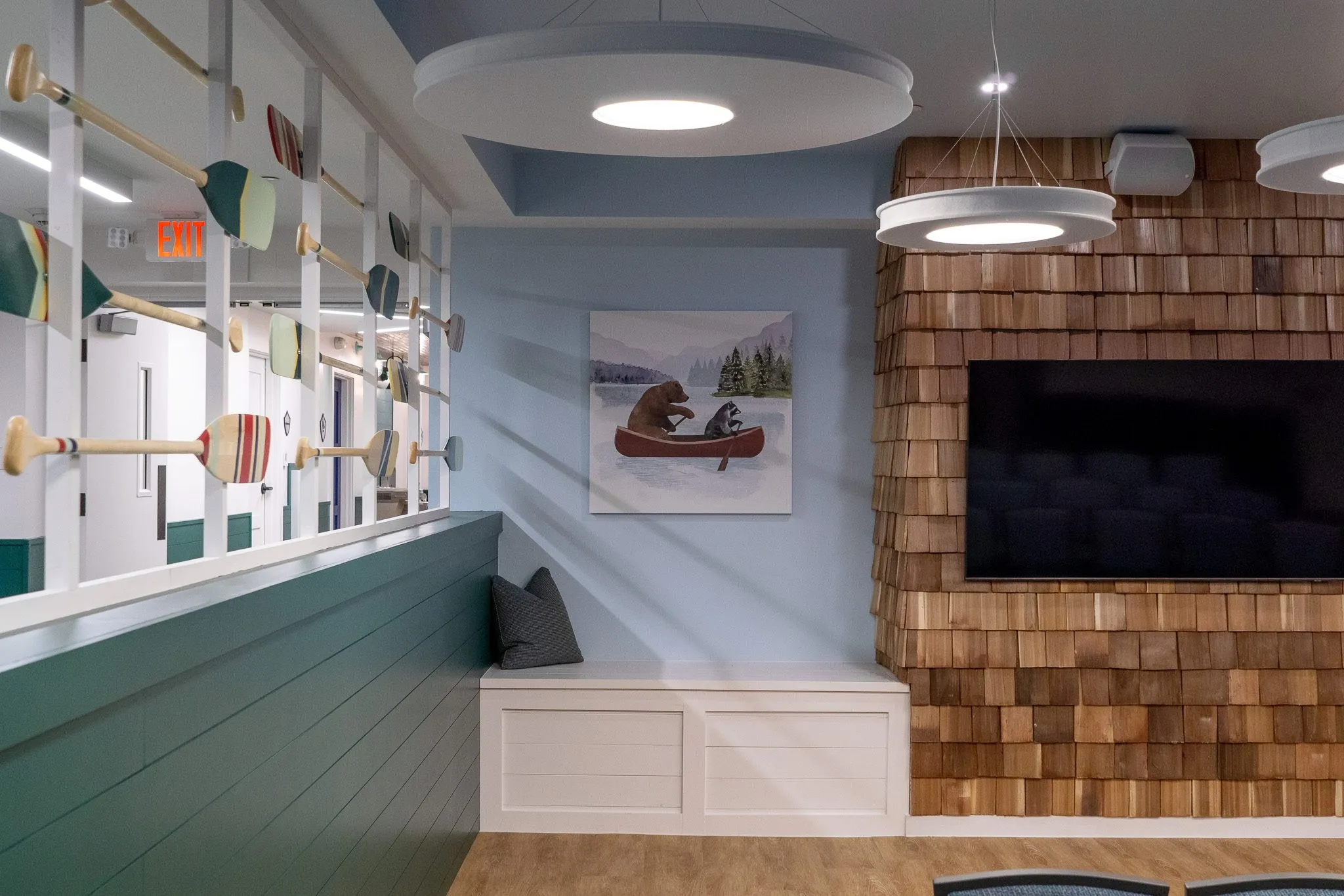 School interior detail: cedar shingle wall with a screen beside a framed canoe painting above a built-in bench