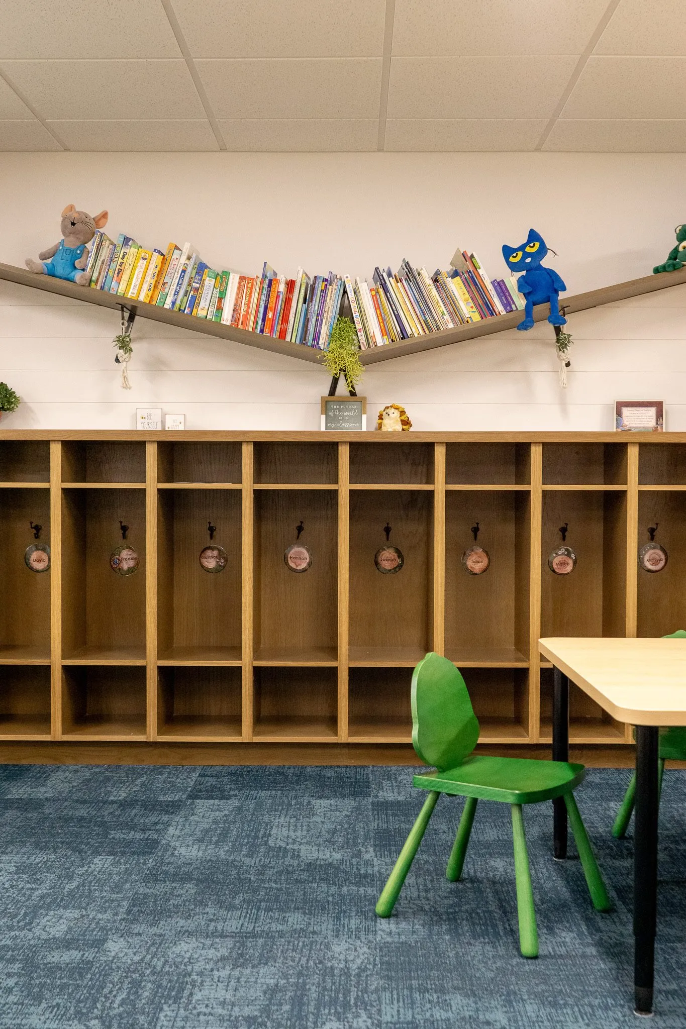 School cubby lockers with coat hooks below angled shelves lined with picture books