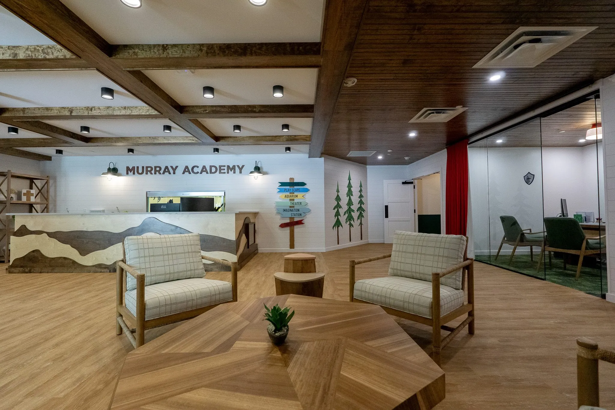 School lobby seating with plaid chairs and stump tables in front of the reception desk and its painted mountain range