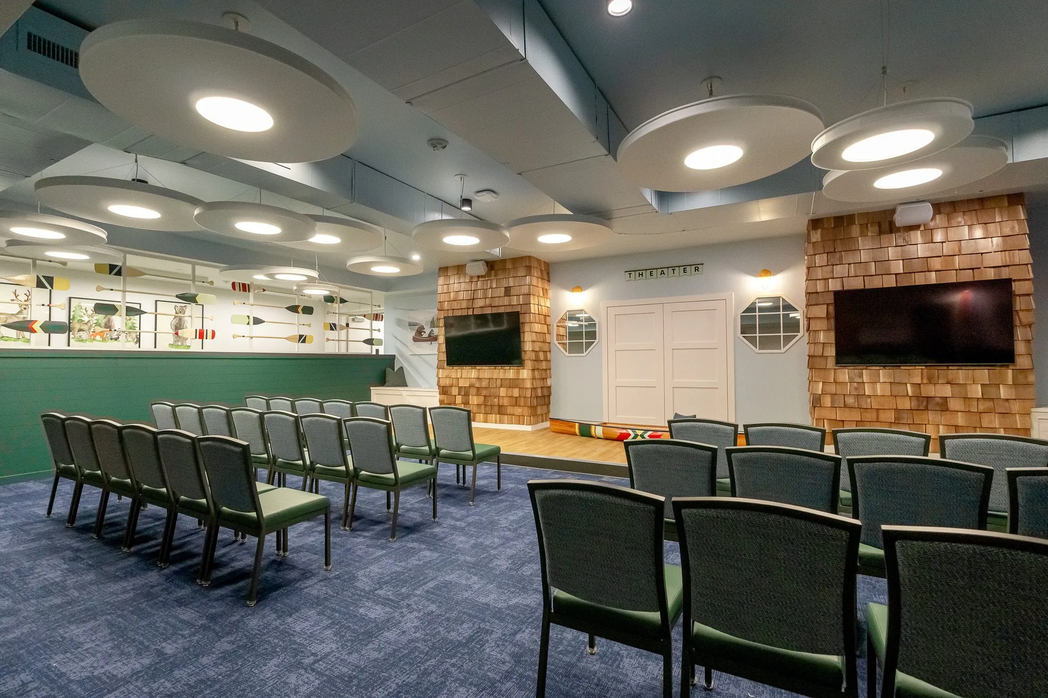 School theater with rows of green chairs facing the cedar shingle wall and its two screens