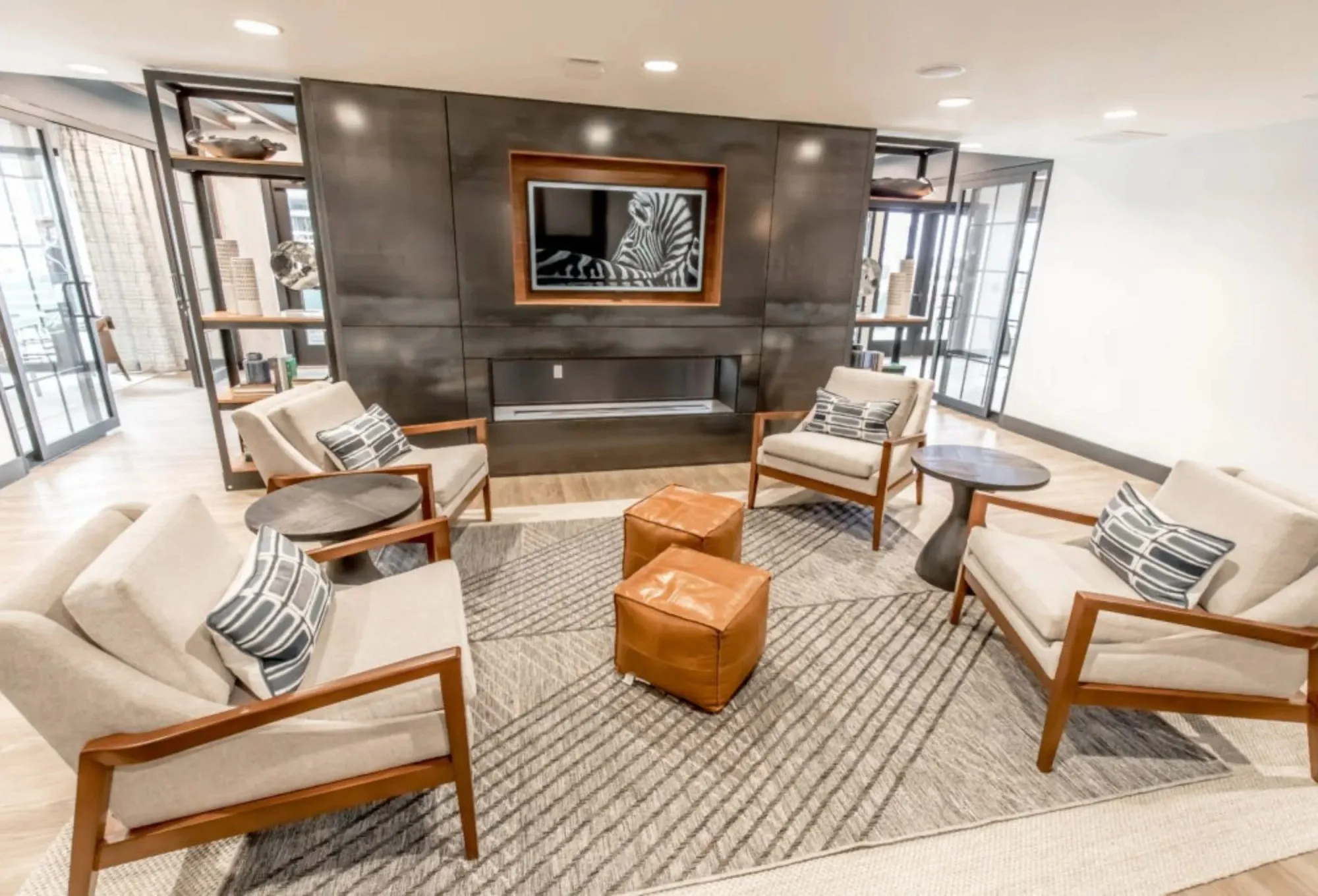 Multifamily amenity fireside seating, four mid-century armchairs around leather ottomans facing a blackened metal fireplace
