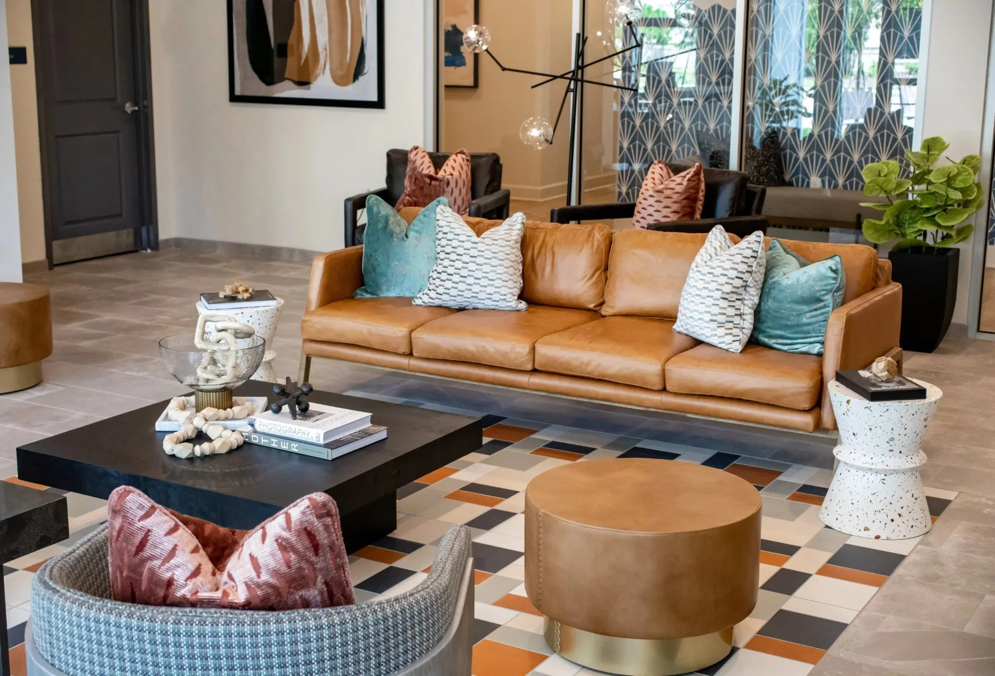 Multifamily amenity lobby with a tan leather sofa, mixed pillows, a black waterfall coffee table and a geometric orange and black tile floor