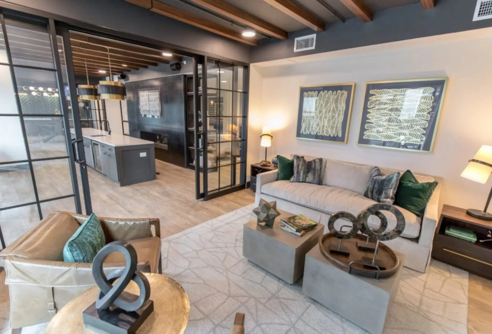 Multifamily amenity clubroom lounge with dark exposed beams, a steel and glass partition to the kitchen and a cream sofa