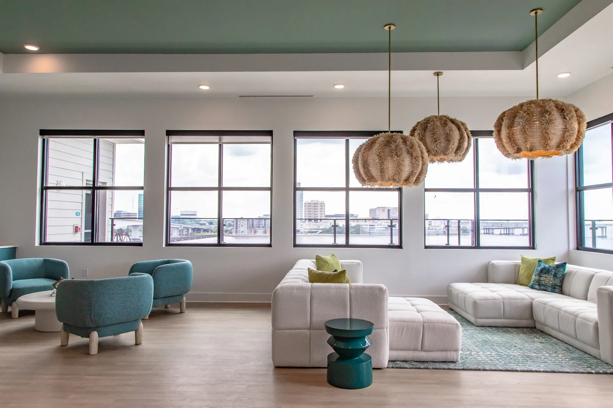 Multifamily amenity clubroom with white modular sectionals, teal barrel chairs and rattan pendants under a green ceiling