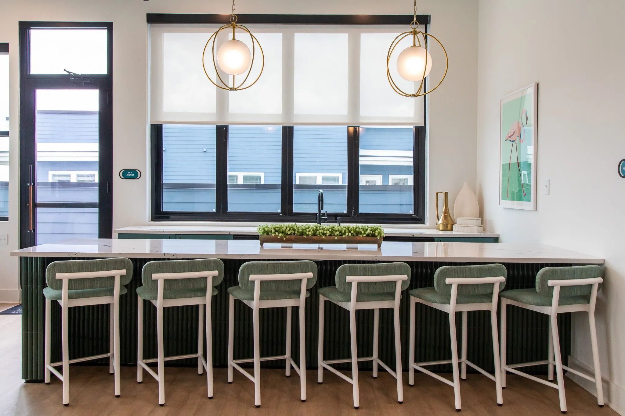 Multifamily kitchen island with green upholstered barstools under brass orb pendants, a flamingo print on the wall
