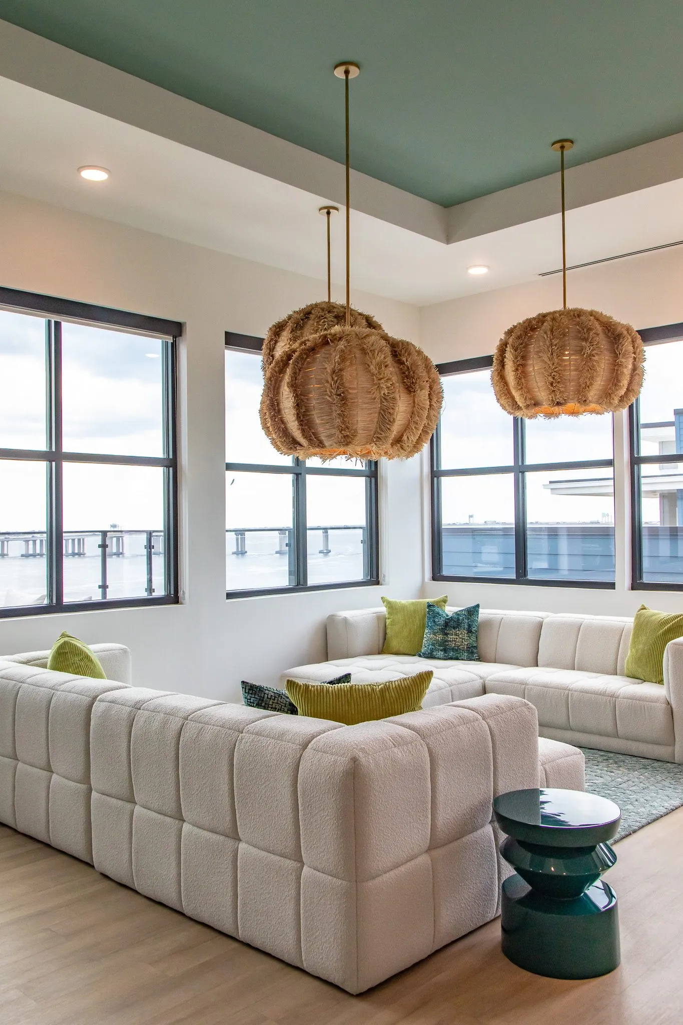 Multifamily amenity clubroom corner with a white modular sectional and teal side table under rattan pendants