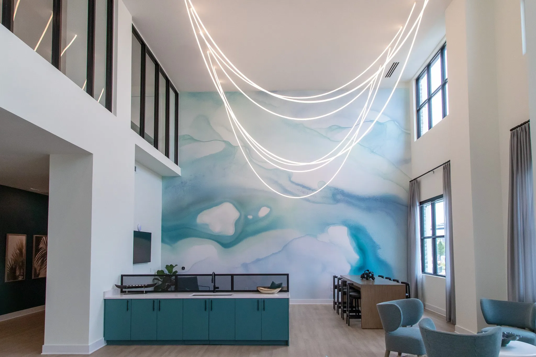 Multifamily amenity two storey lounge with a blue watercolor mural, teal cabinetry and a sculptural looping light overhead